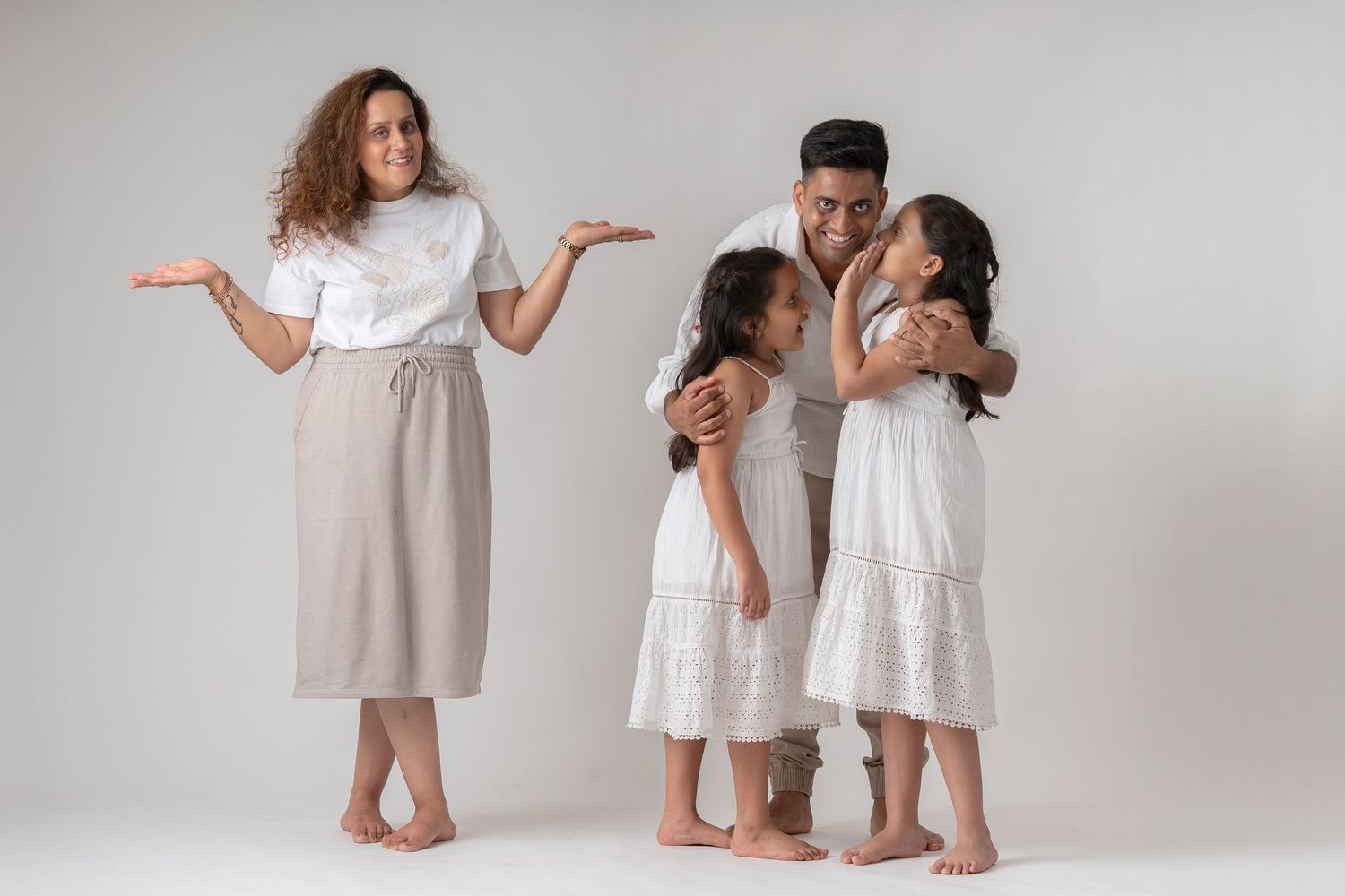 Family of four in white outfits with mother gesturing playfully in a bright studio photo.