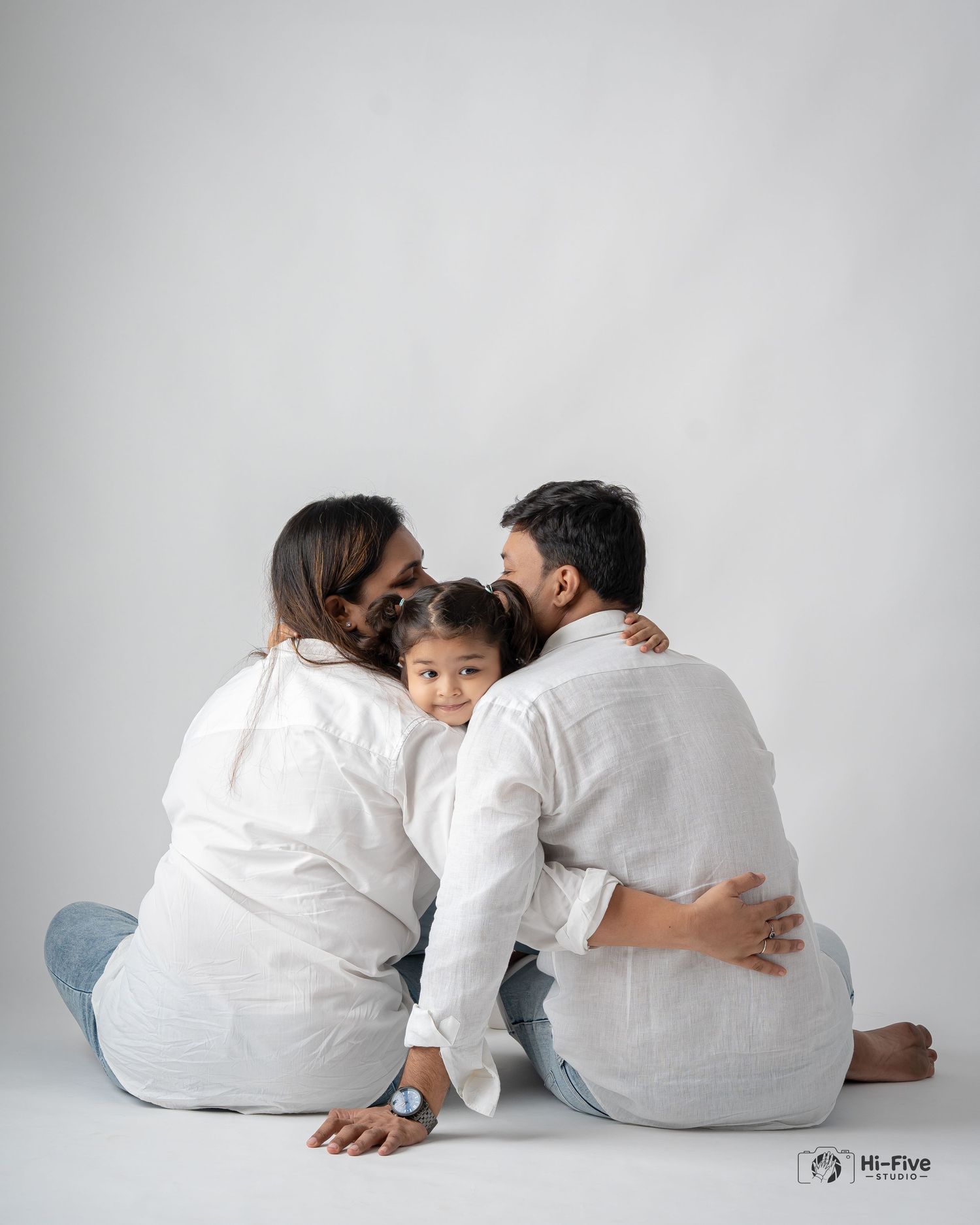 Family of three sitting on floor from behind, parents kissing young child in middle.