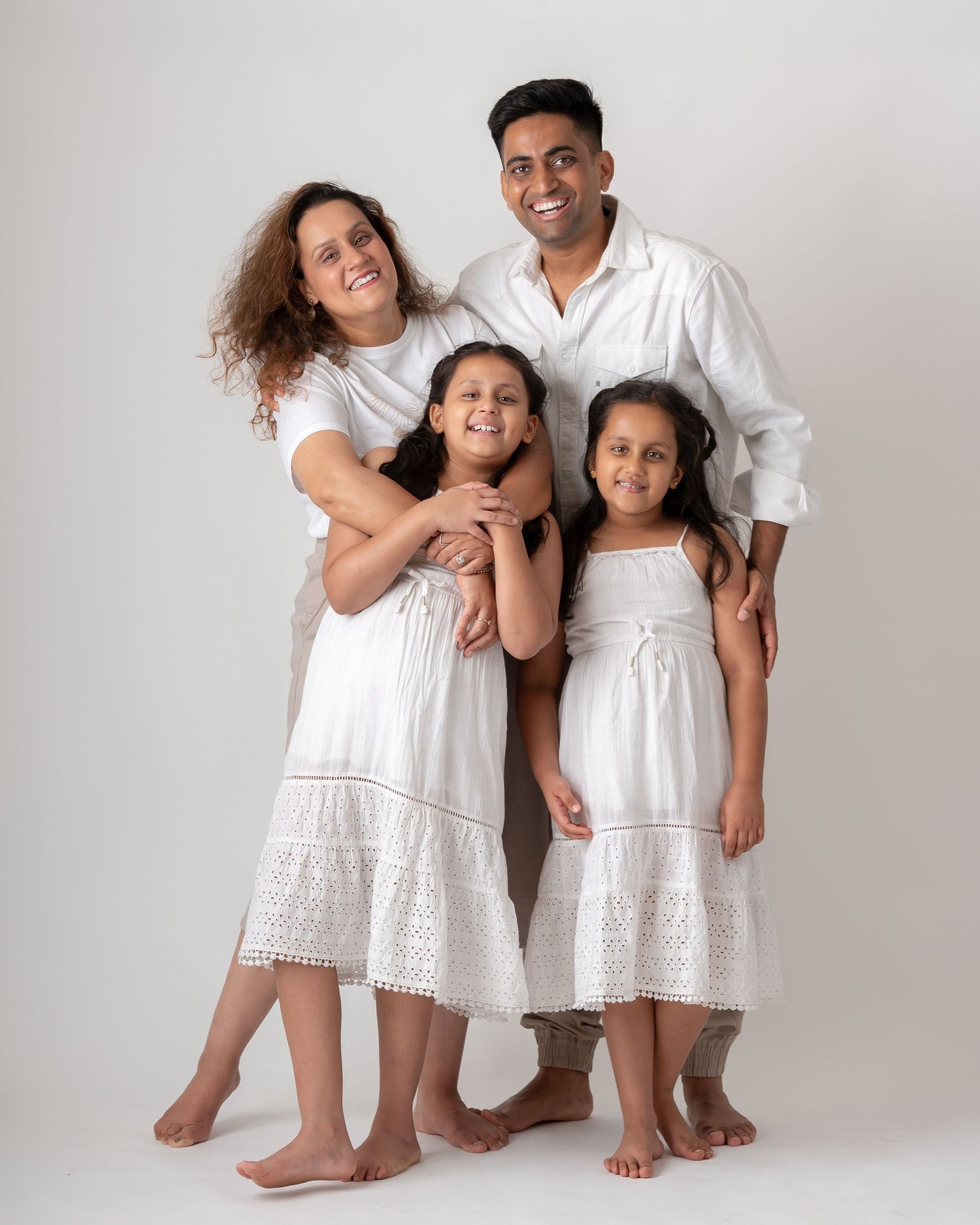 Smiling family of four in white outfits embracing together in a professional studio portrait.