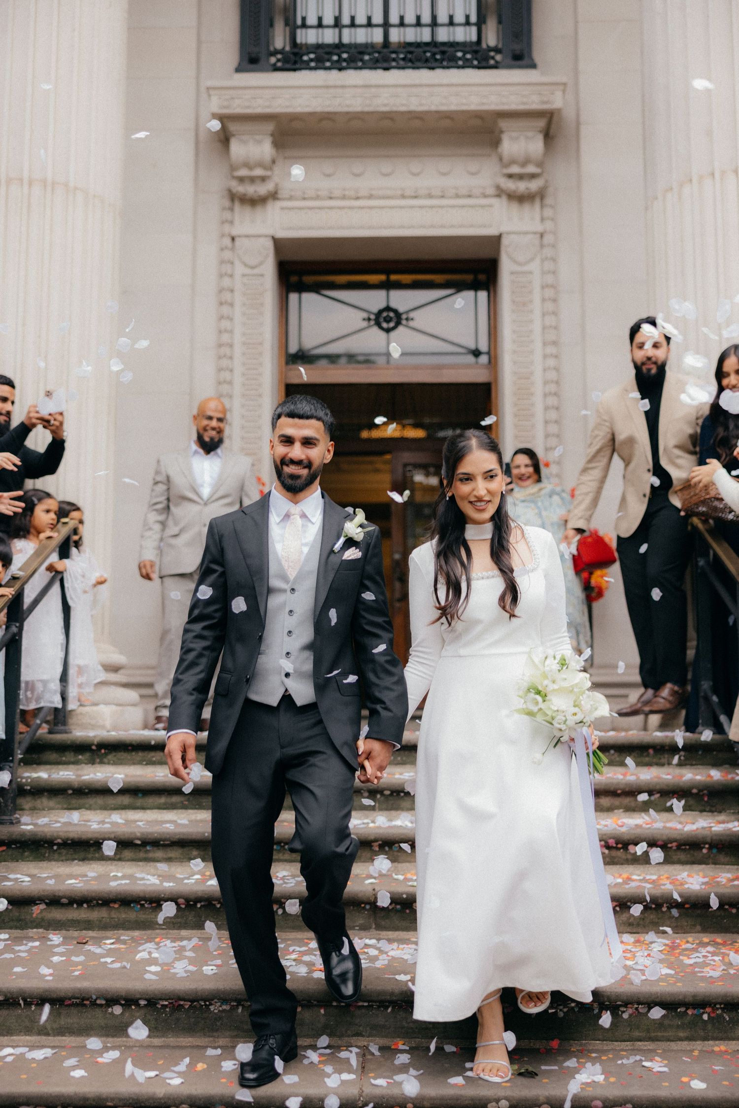 Wedding party celebrating on grand steps with confetti flying through the air.