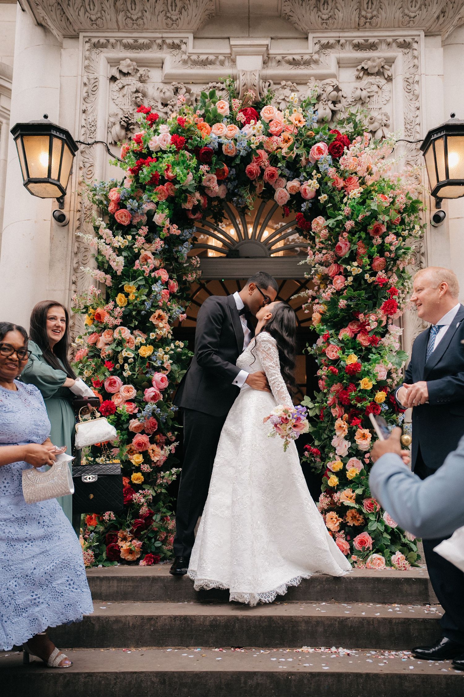 Wedding party celebrates with joy under an elaborate rose-covered archway.