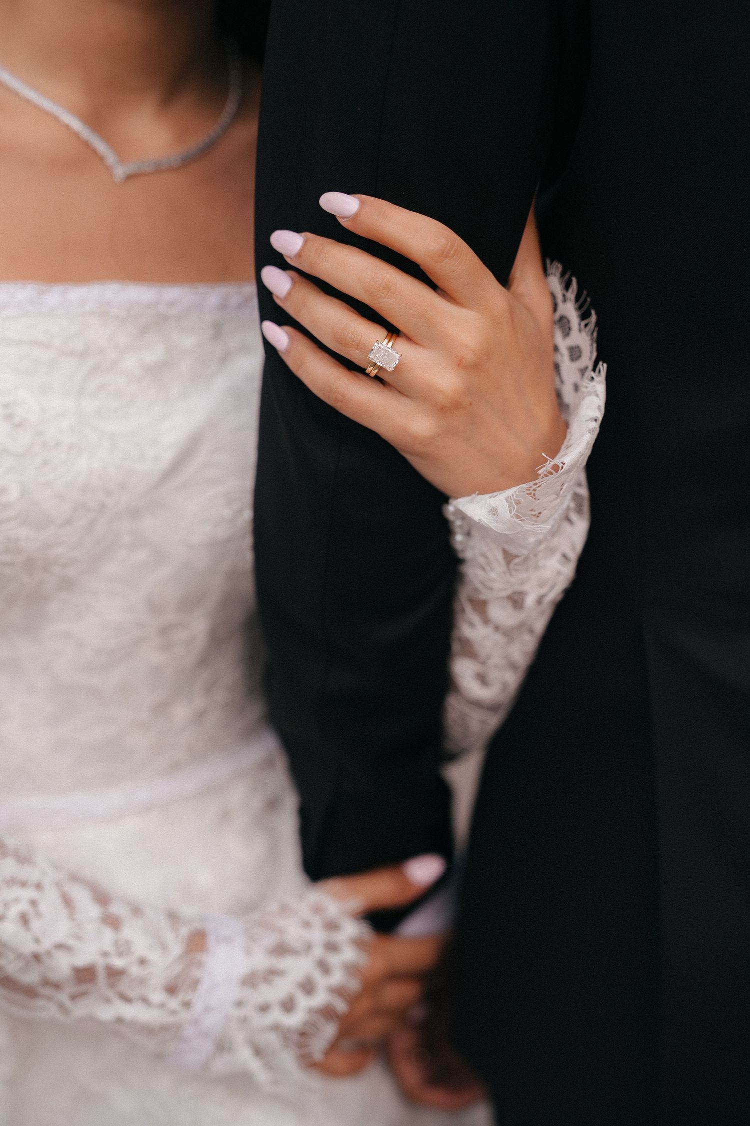 Close-up details of wedding attire showing lace sleeves, engagement ring, and formal wear.
