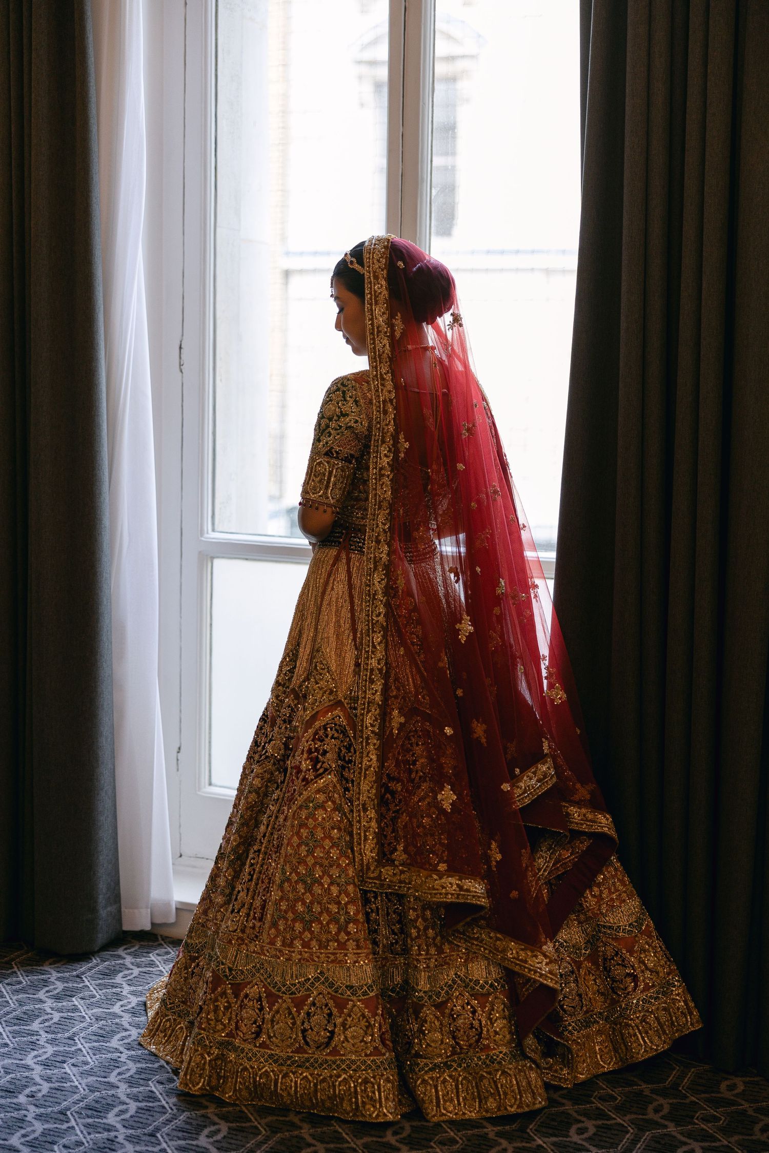 Ornate red and gold lehenga dress shown in elegant window lighting.