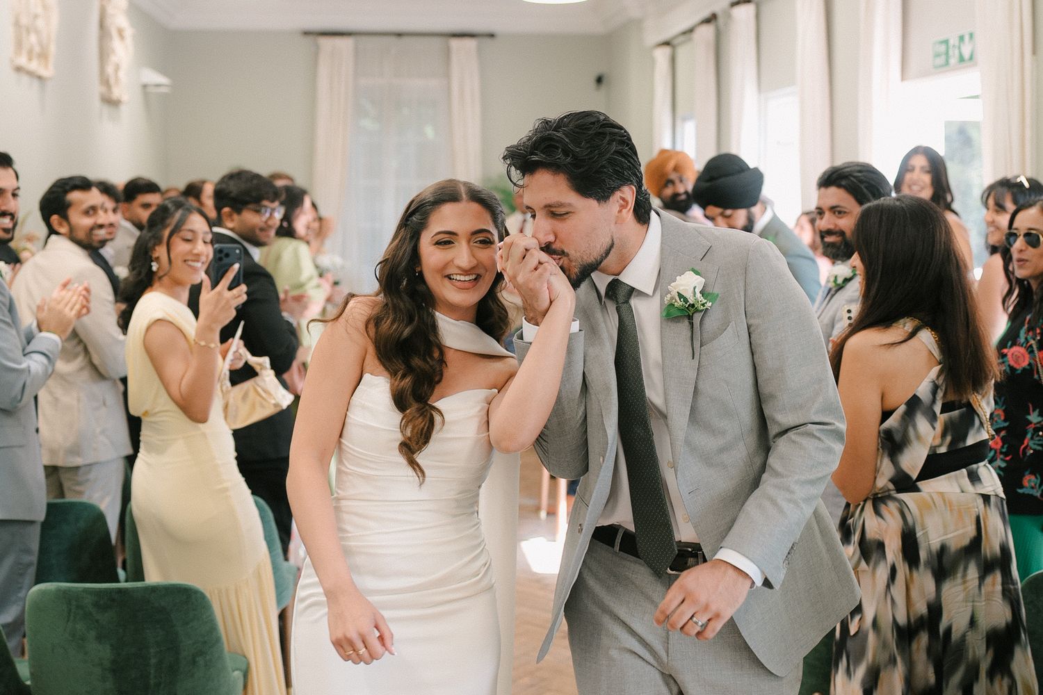 Bride and groom share a joyful moment walking down the aisle surrounded by smiling wedding guests.