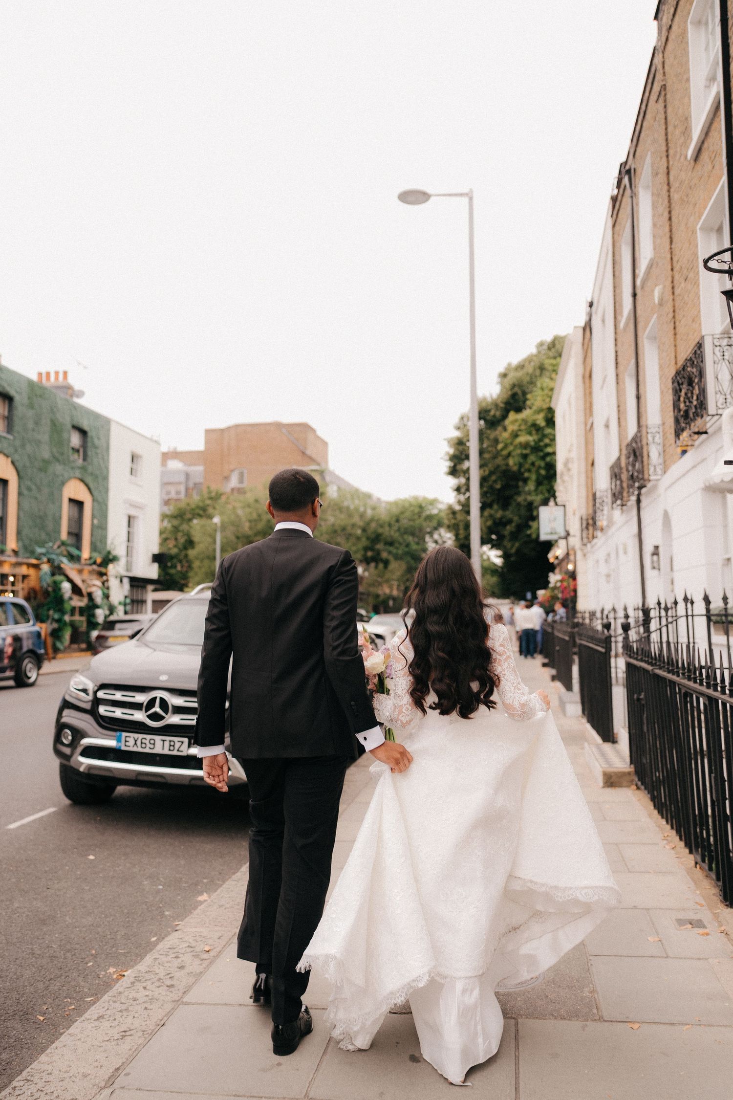 Wedding couple walks down city street holding dress train.