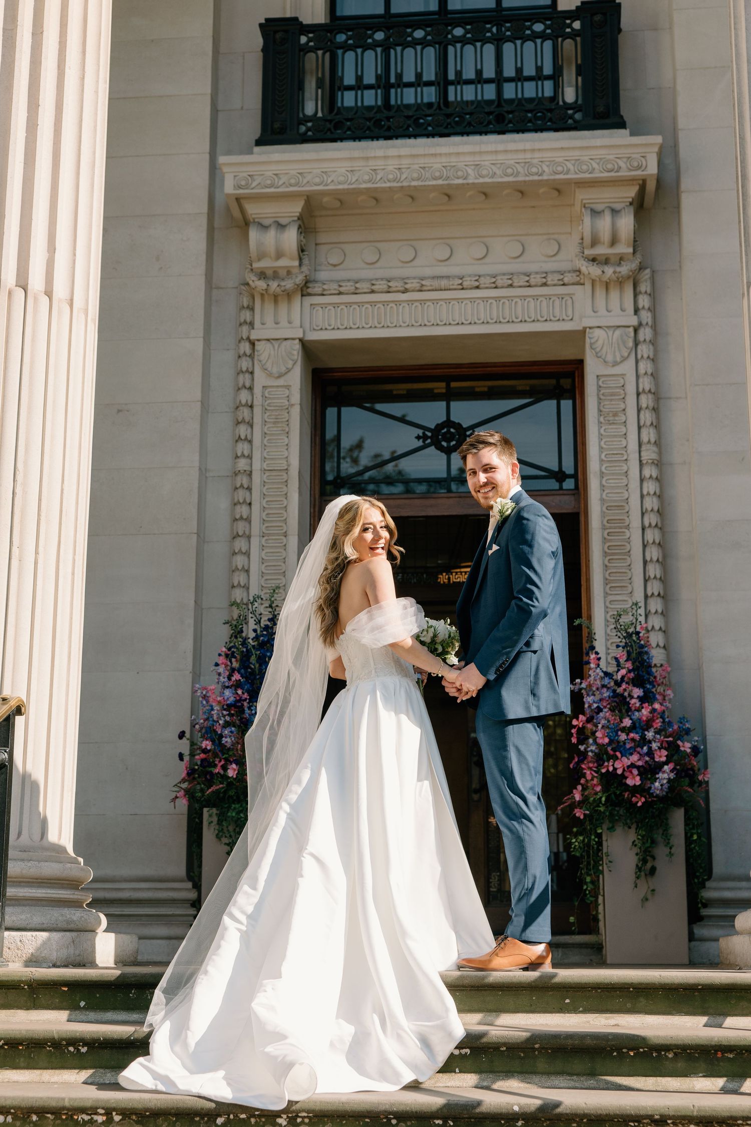 Elegant wedding photos captured outside a grand building with classical columns and floral arrangements. Old Marylebone Townhall