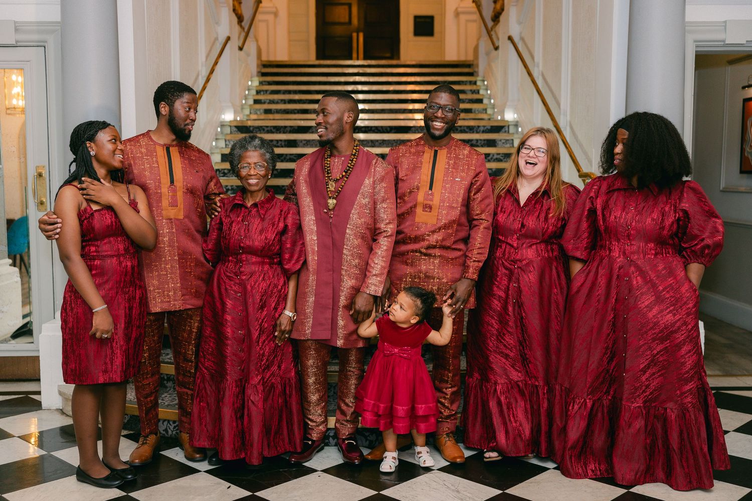 Wedding party members wearing coordinated burgundy outfits standing together in a formal venue.