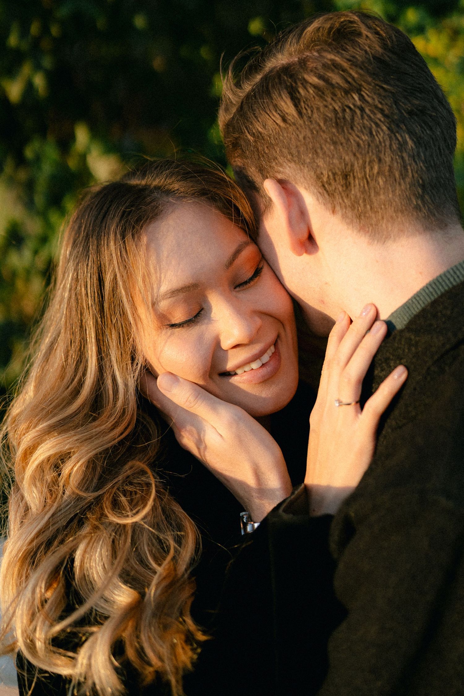 A couple shares an intimate moment while laughing together in natural lighting.