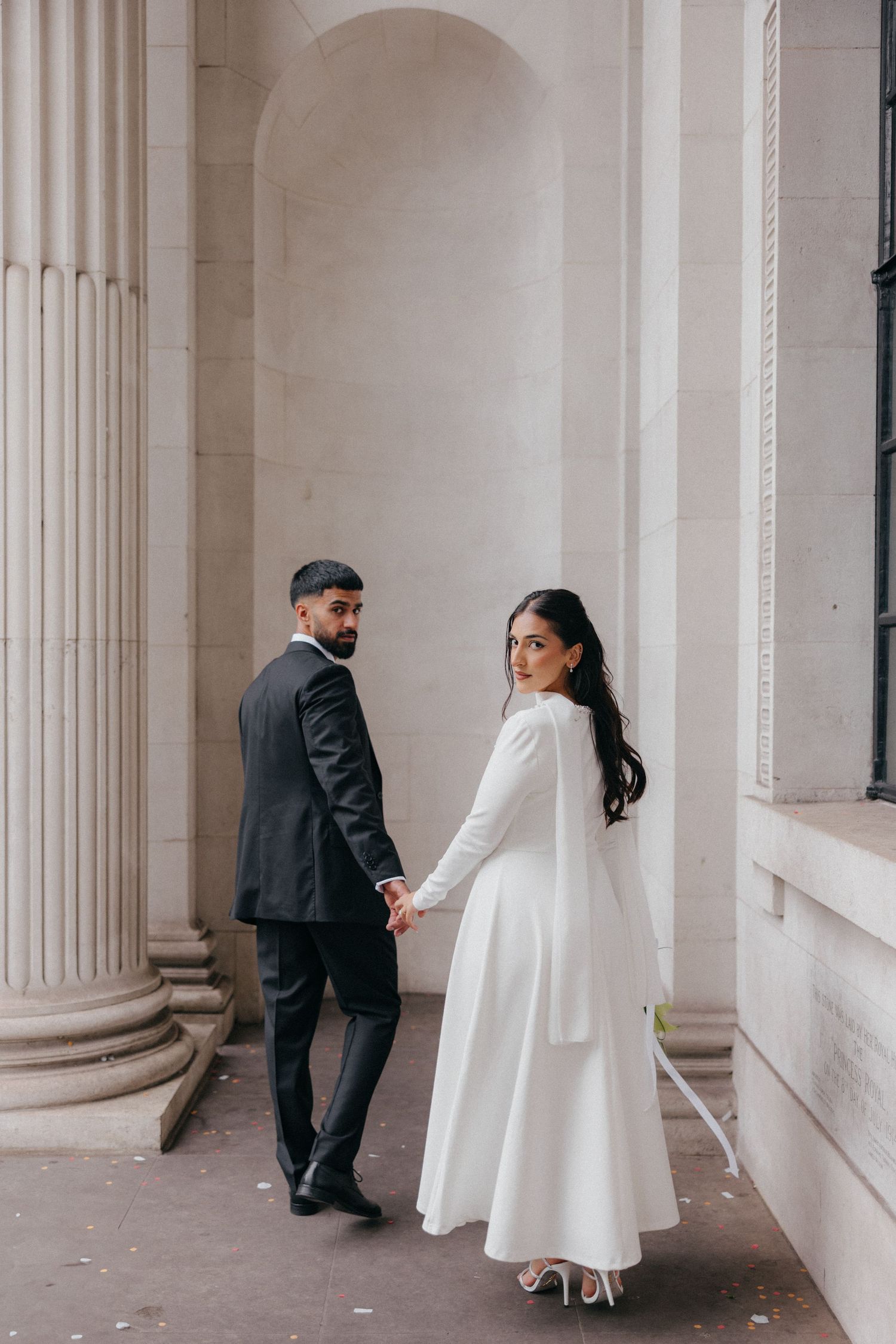 A bride and groom share playful moments between elegant white columns in a classic architectural setting.