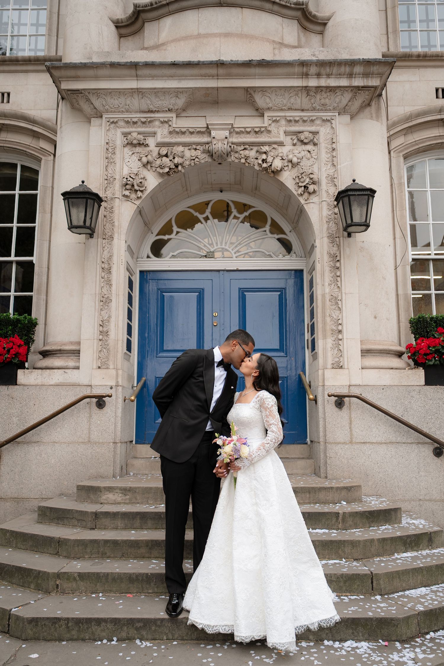 Wedding couple posing in front of an ornate building entrance with blue doors.