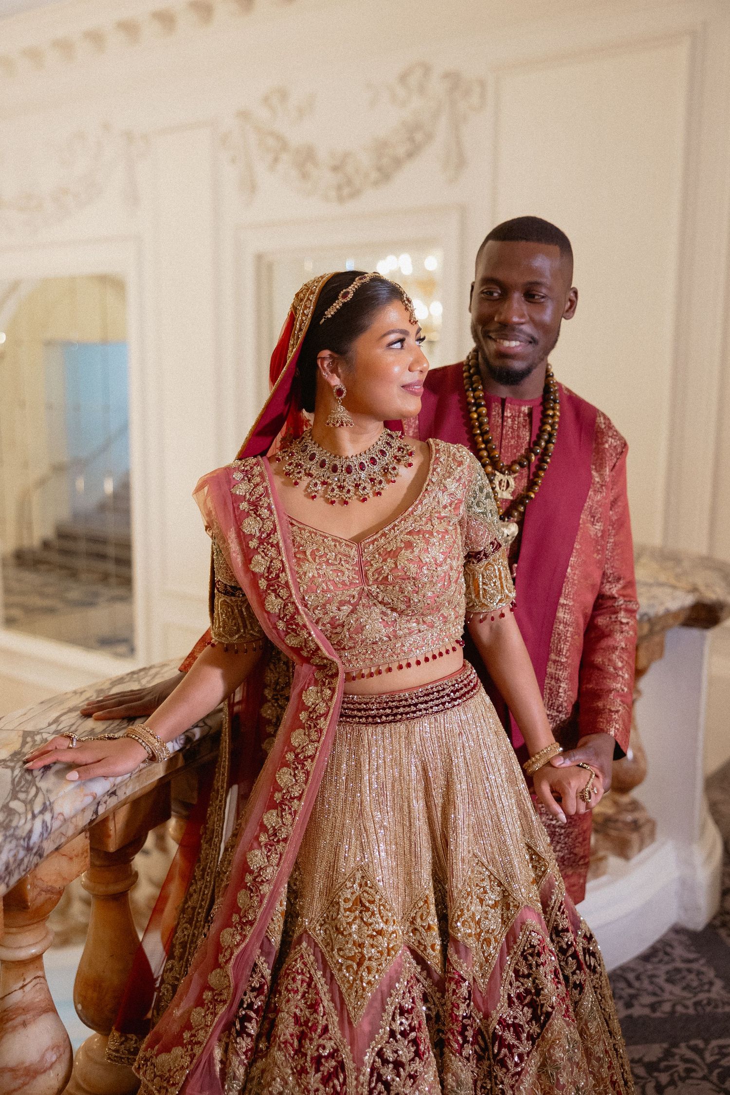 A couple in traditional Indian wedding attire shares joyful moments together in an elegant indoor setting.