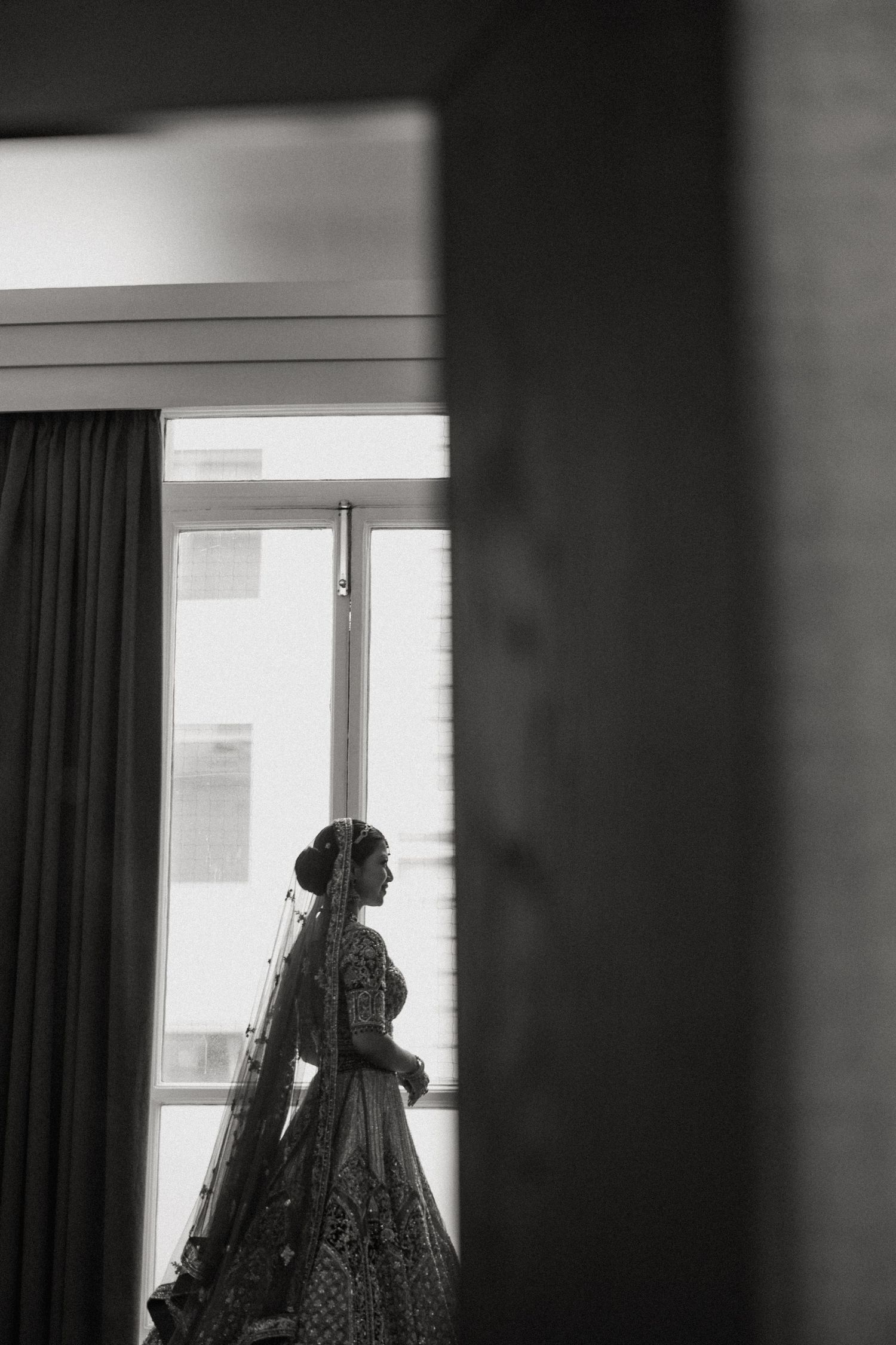 Silhouette of a bride in traditional attire standing by a window in black and white.