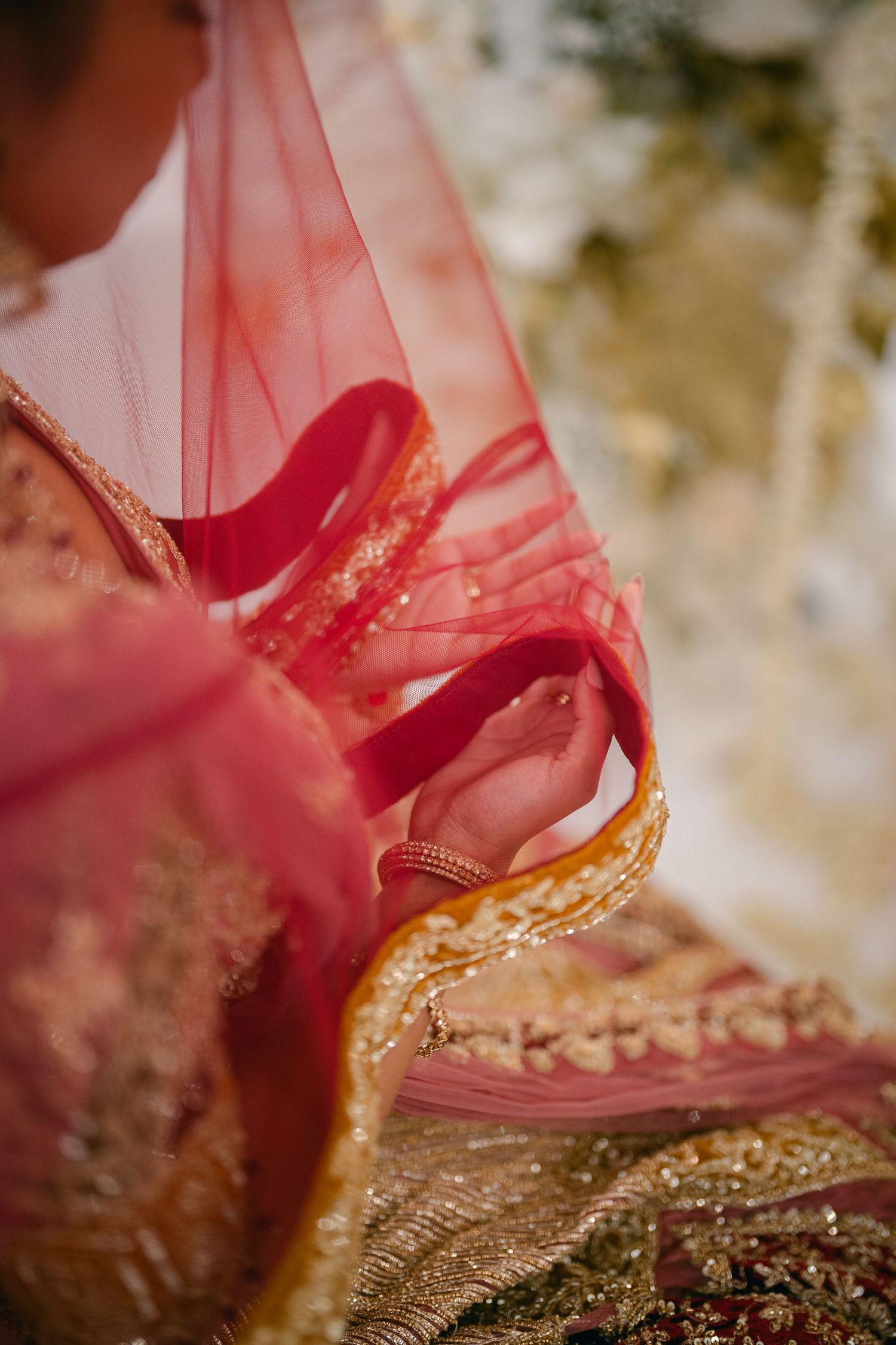 Close-up detail of a red and gold traditional Indian wedding shoe with intricate embroidery on textured surface.