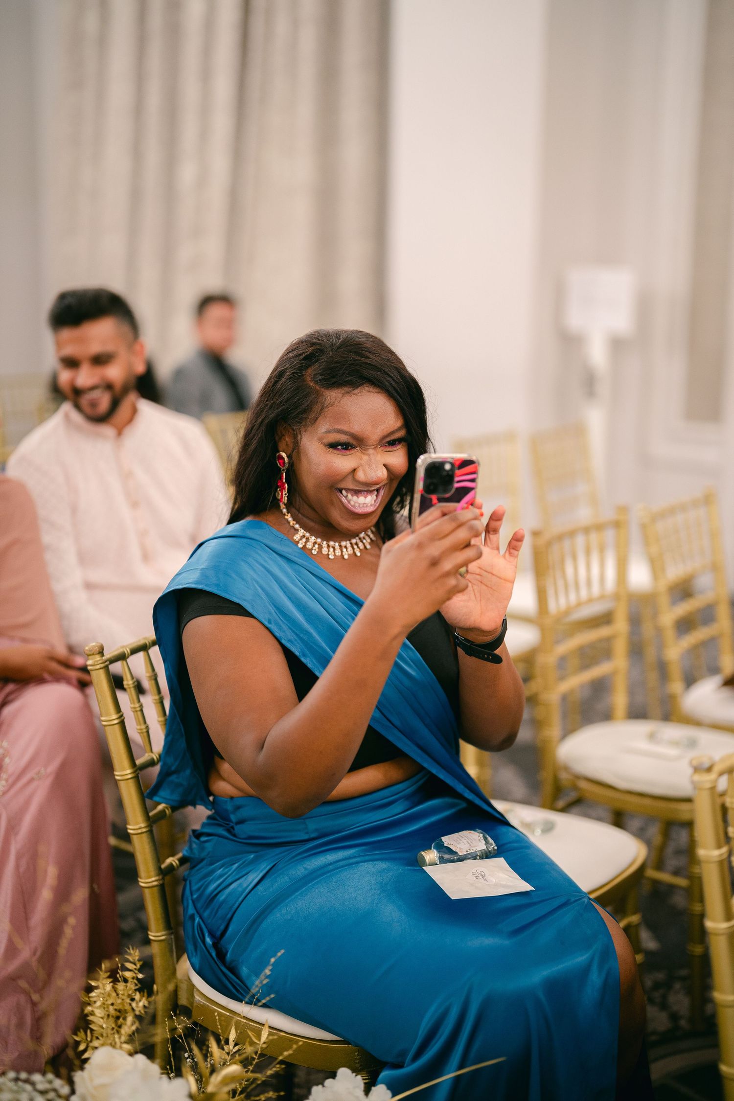 Wedding guests in blue attire laughing and enjoying themselves at an elegant reception with gold chairs.