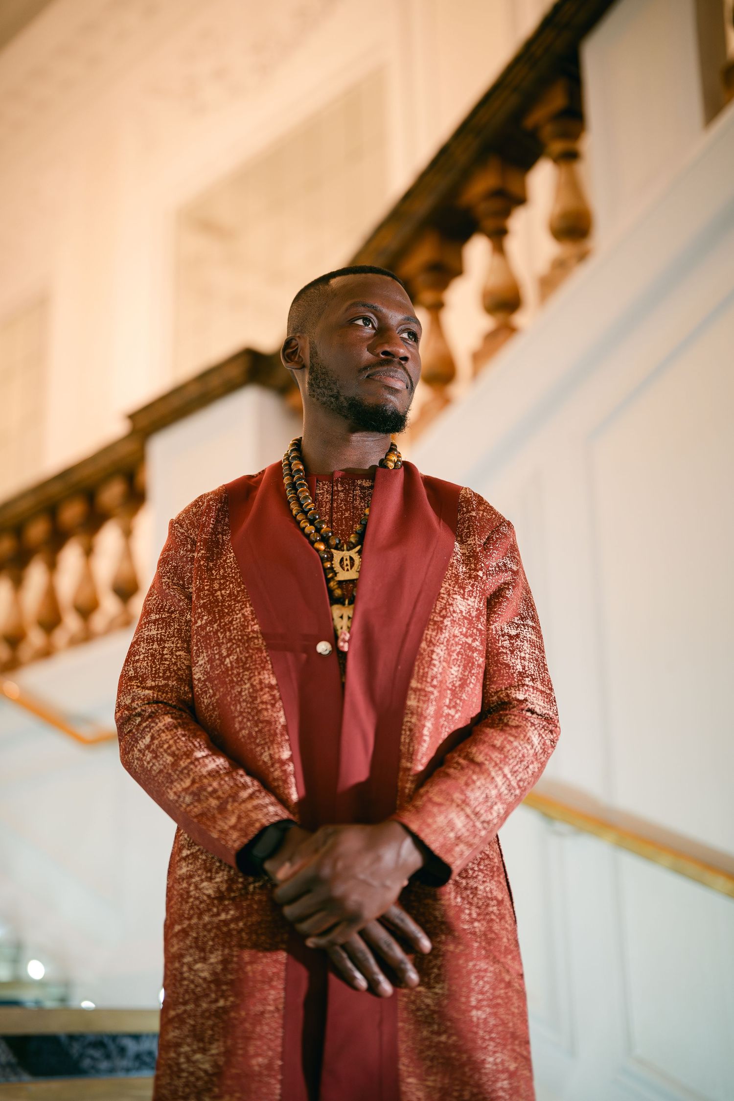 A person wearing a luxurious red and gold brocade suit jacket stands elegantly against a light-colored interior.