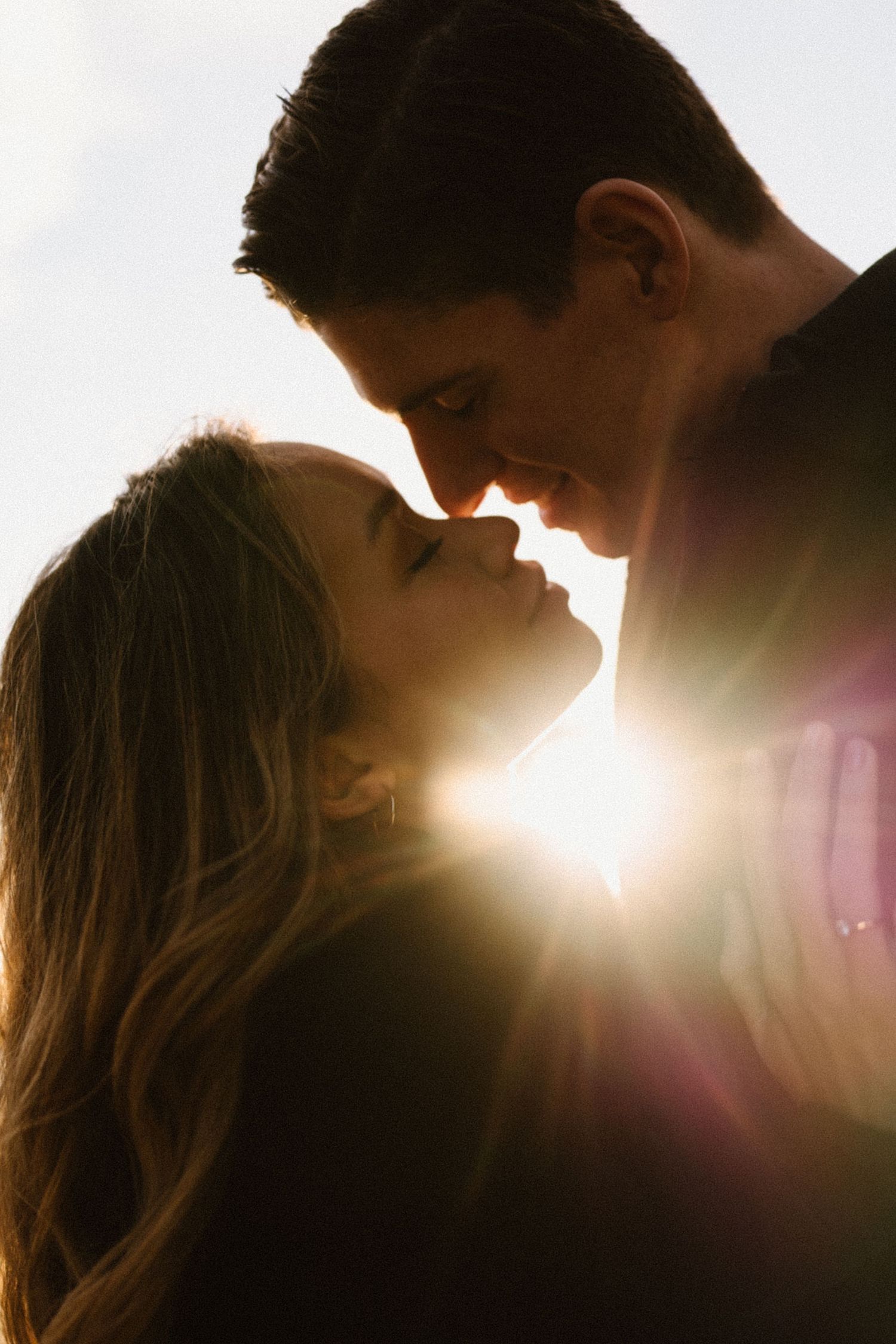 A silhouetted couple shares a tender moment with sun flare creating a dreamy atmosphere.
