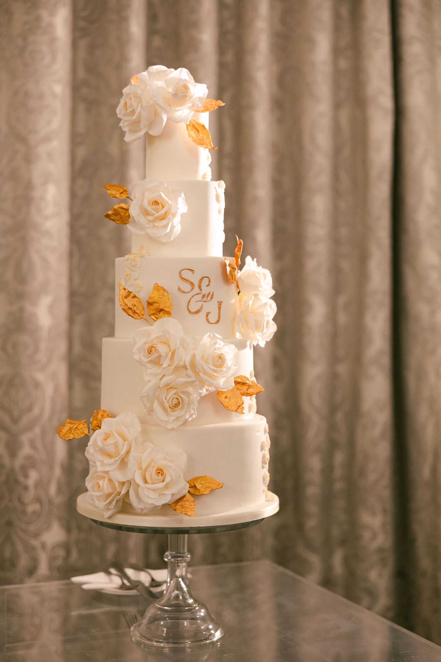 Elegant white wedding cake decorated with sugar roses and gold butterfly accents.
