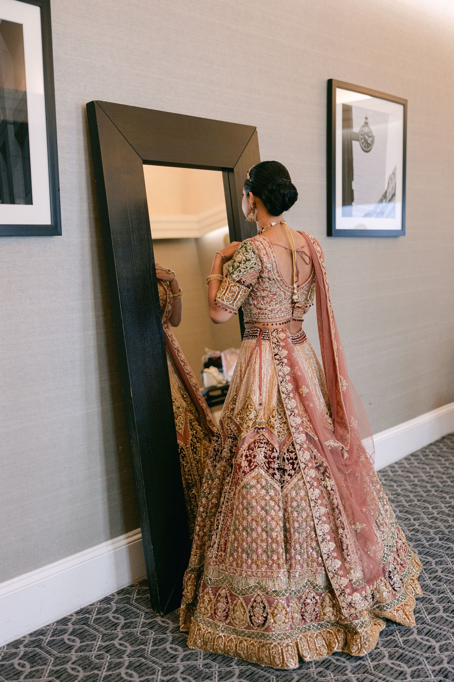 Traditional pink and gold embroidered lehenga dress displayed in a hotel hallway with patterned carpet.