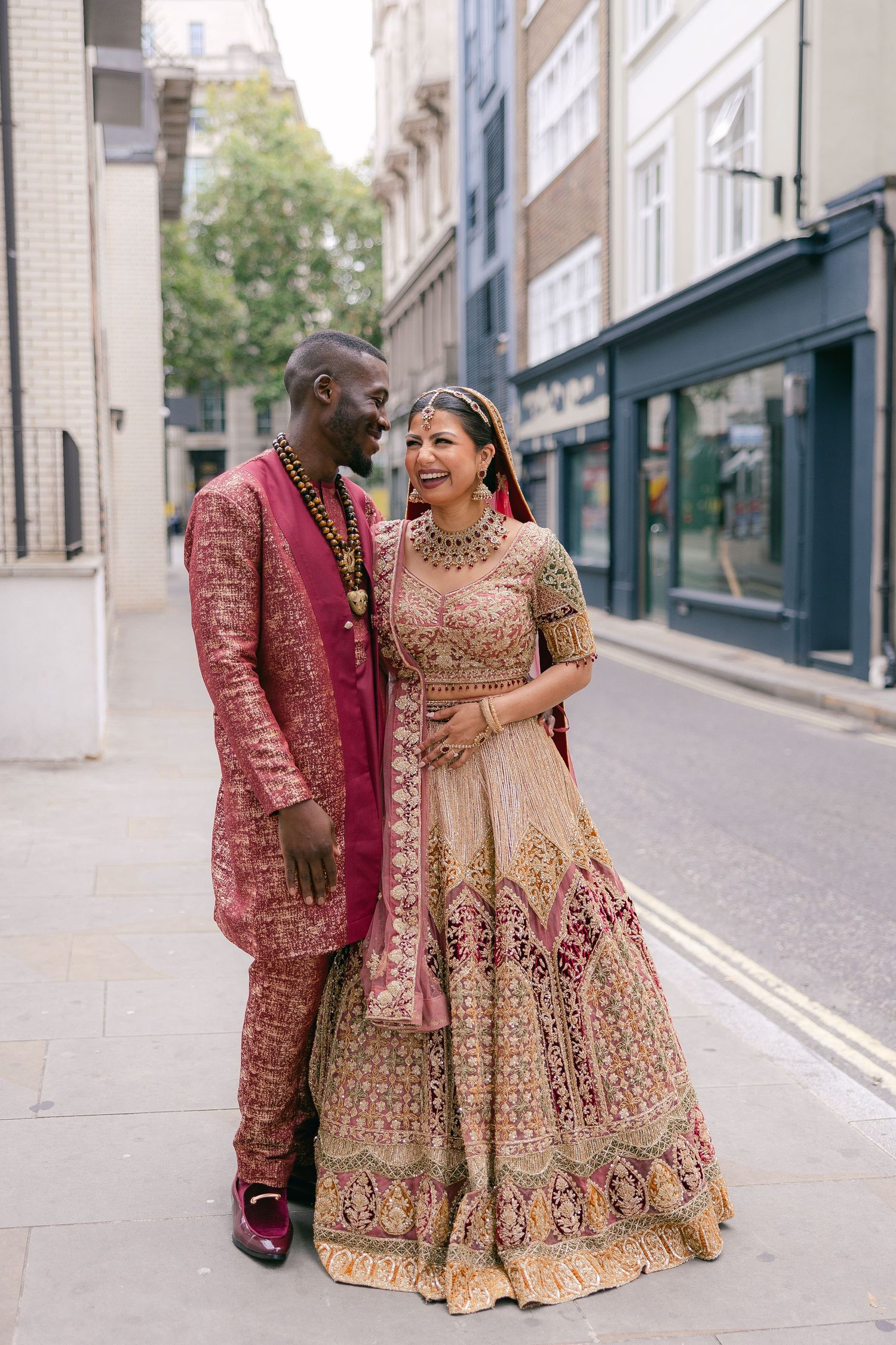 Couple in matching red and gold traditional Indian wedding attire photographed on a quiet city street.