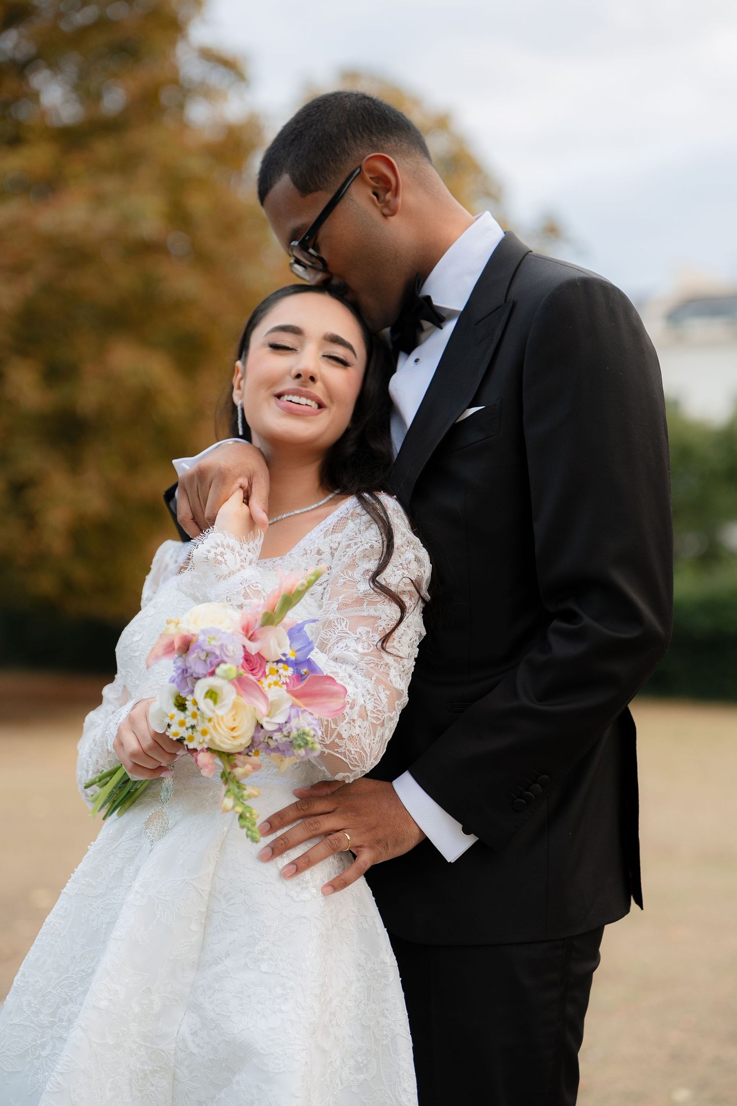 Couple in wedding attire sharing romantic moment in autumn park with colorful bouquet.