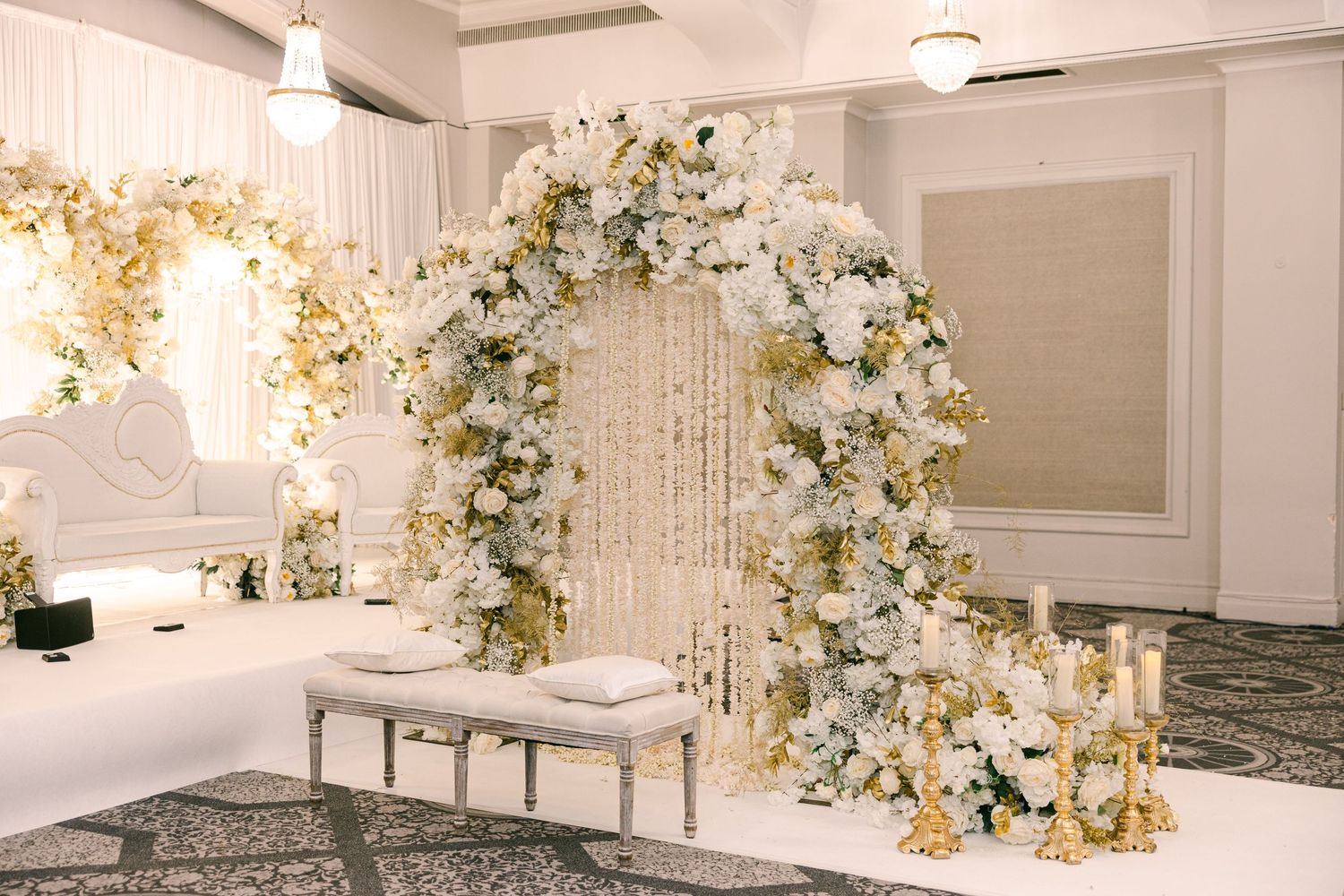 Elegant white wedding reception venue decorated with crystal chandeliers and floral arrangements in cream and gold tones.