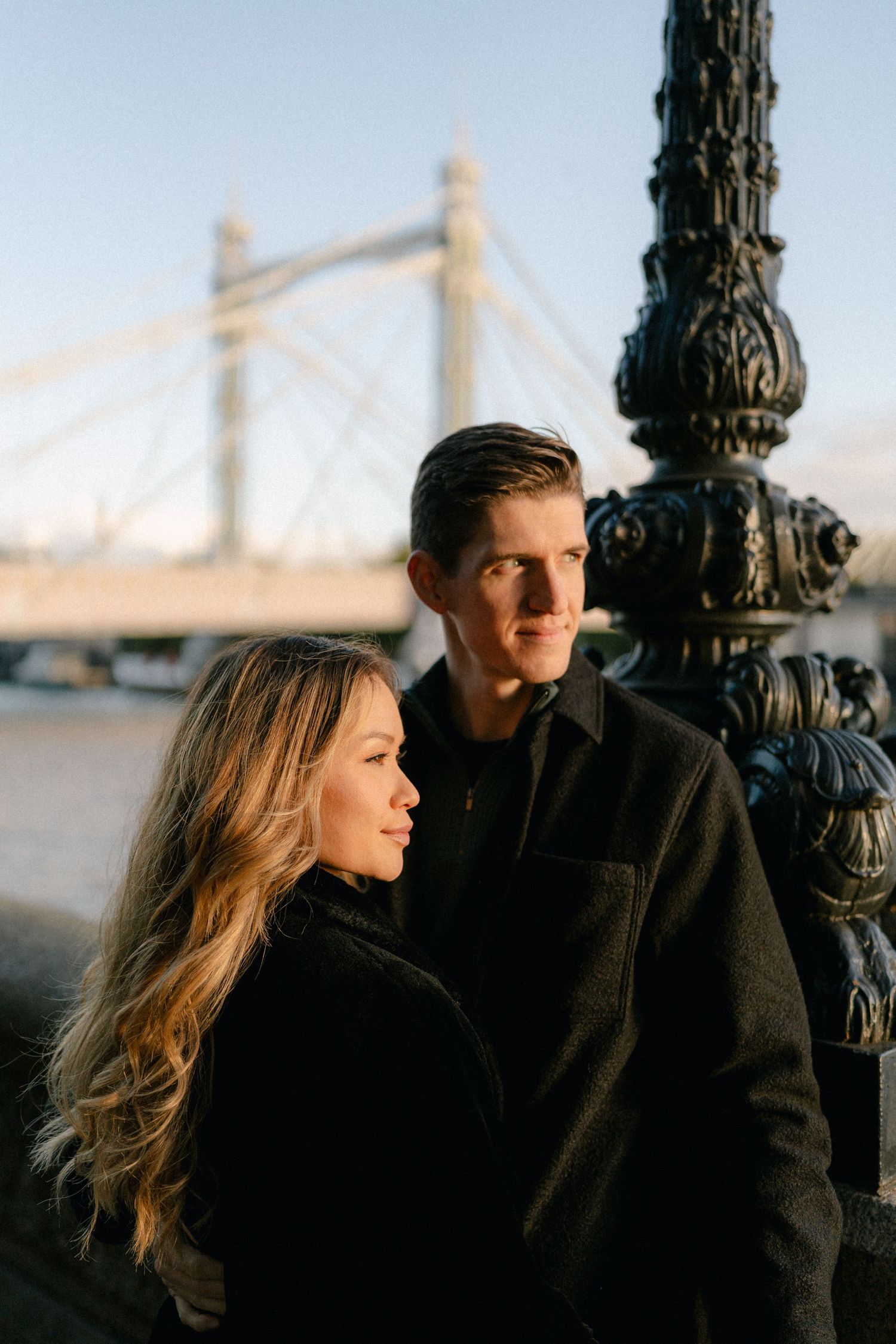 A romantic couple shares an intimate moment against an ornate lamp post during golden hour.