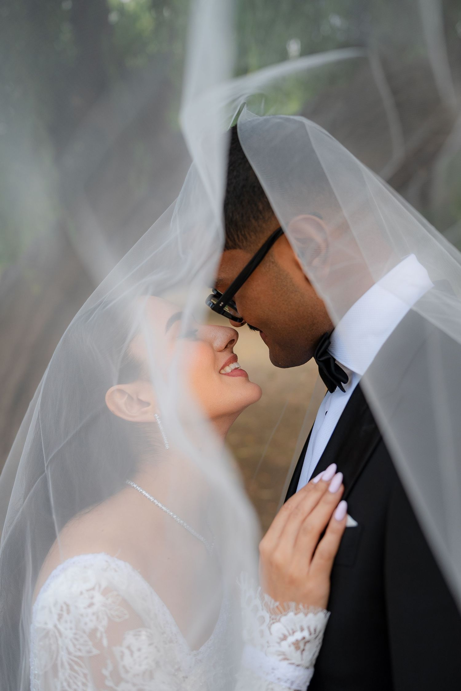 Romantic wedding couple sharing intimate moments under a flowing white veil in an outdoor setting.