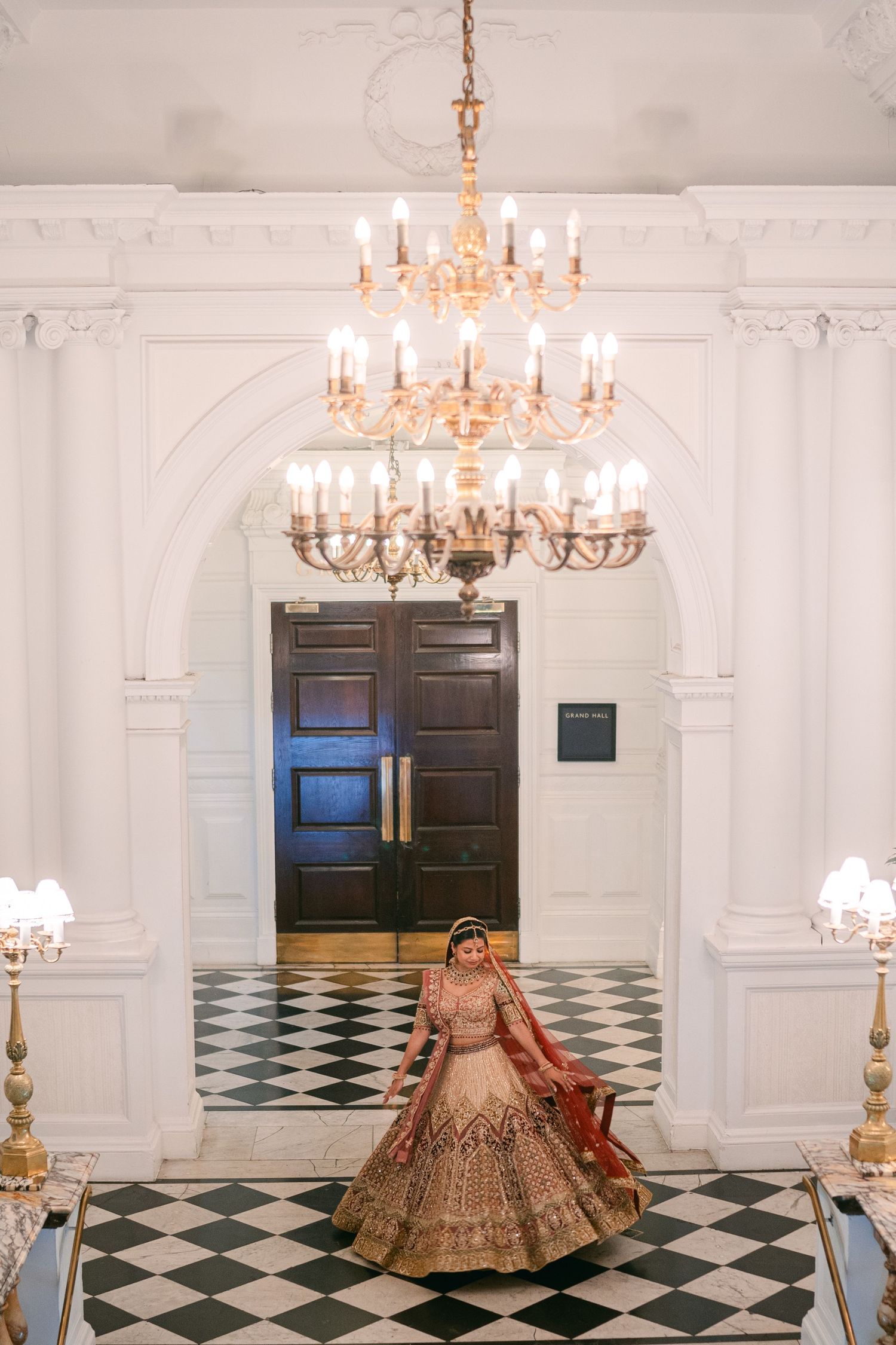 Ornate crystal chandelier illuminates elegant hallway with black and white checkered marble floor and grand archway.