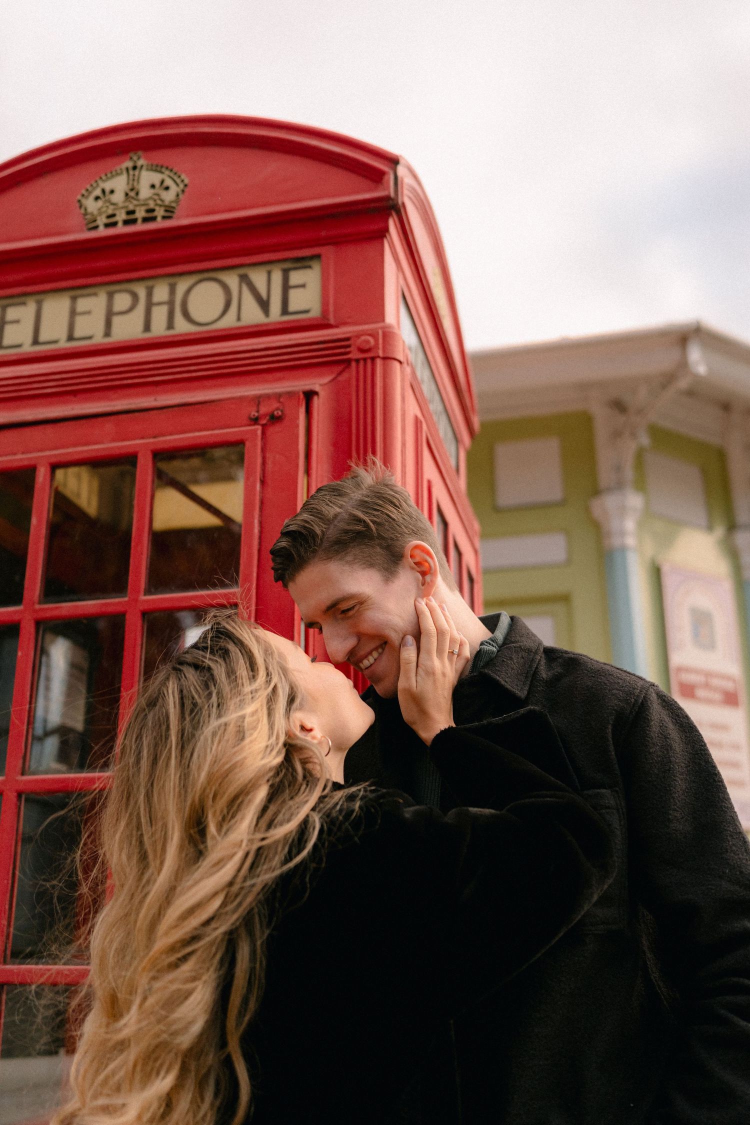 Romantic couple sharing an intimate moment near a classic red London telephone booth.