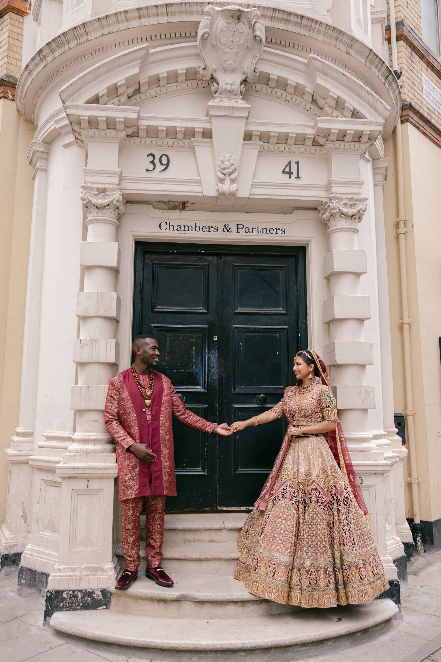 Architectural entrance with ornate white stone details and black doors showing couple in traditional wedding attire.