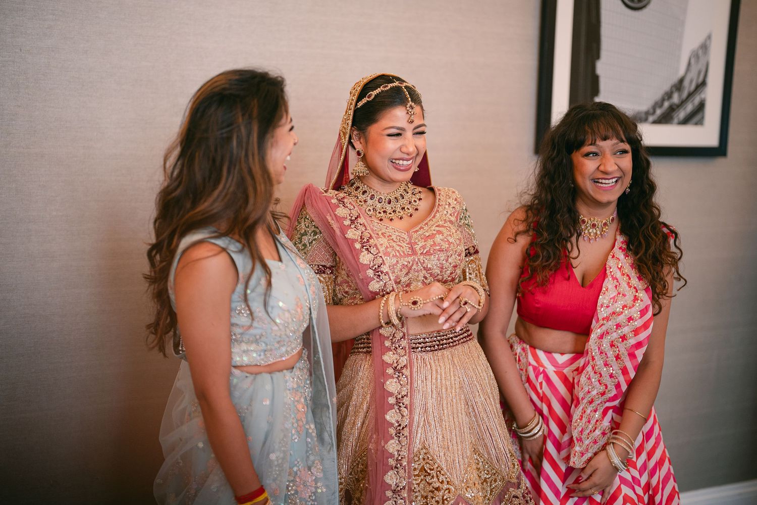 Group of bridesmaids in pastel and pink dresses laughing together during wedding preparations.