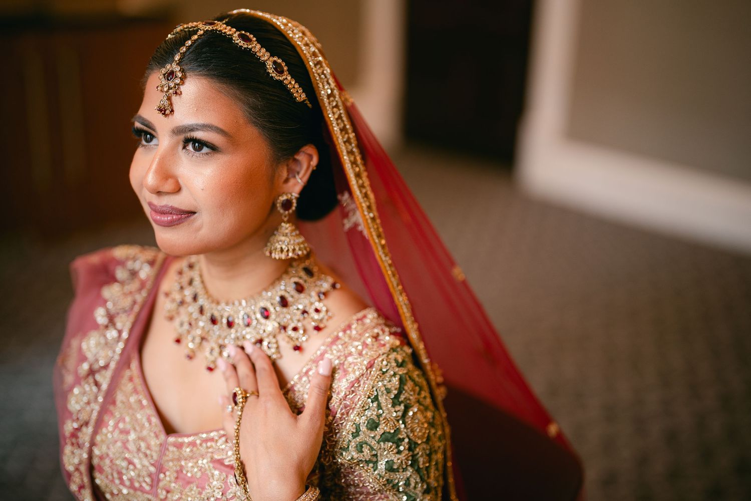 Traditional South Asian bride wearing ornate red and gold wedding attire with elegant jewelry and a red veil.