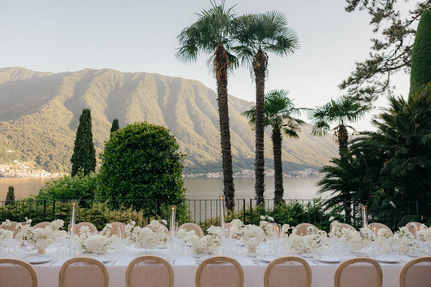 Lakeside wedding reception setup with mountain views and palm trees creating a luxurious outdoor dining space.