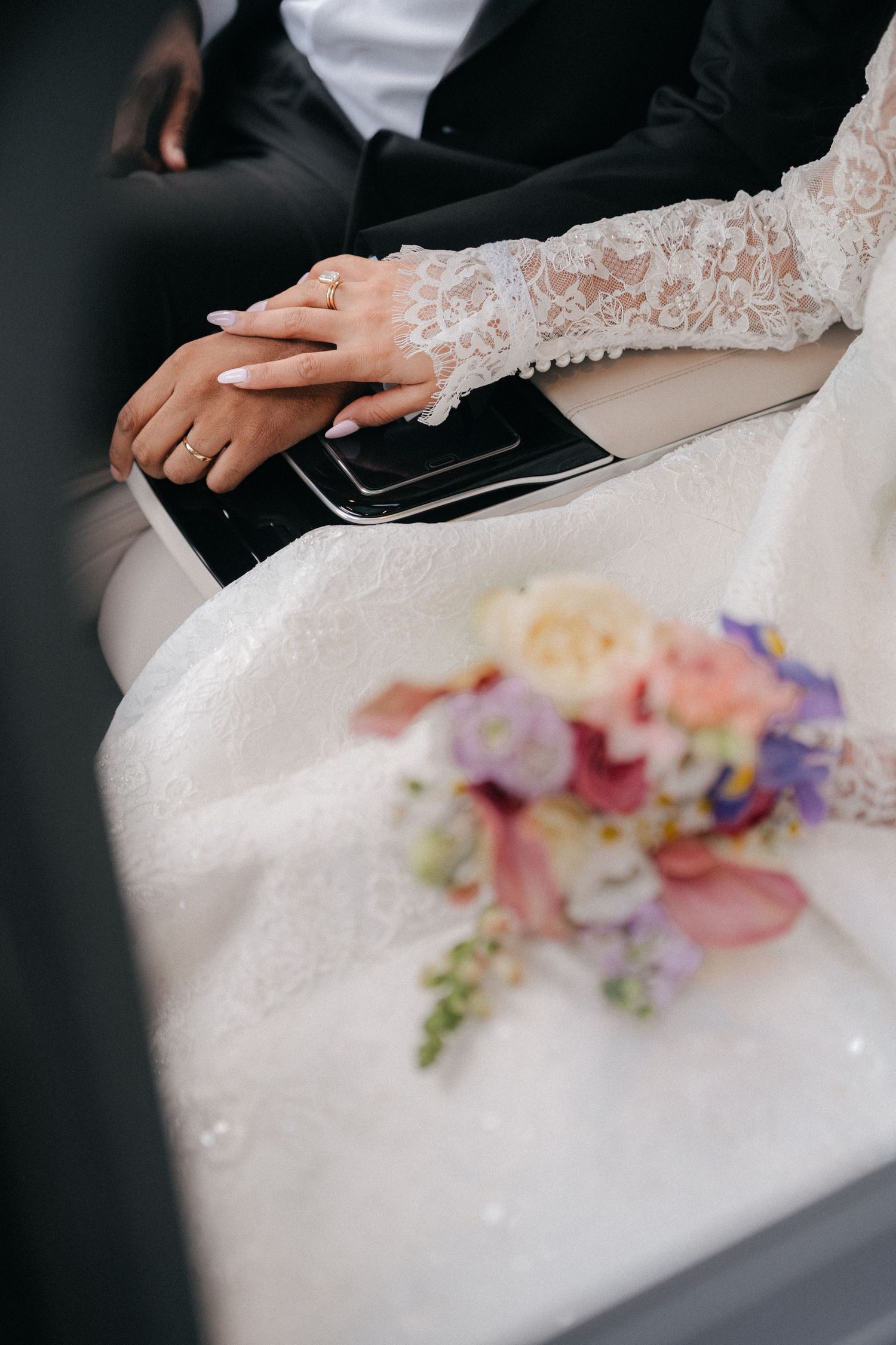 Detail shot of wedding dress lace and colorful floral bouquet resting on white fabric.