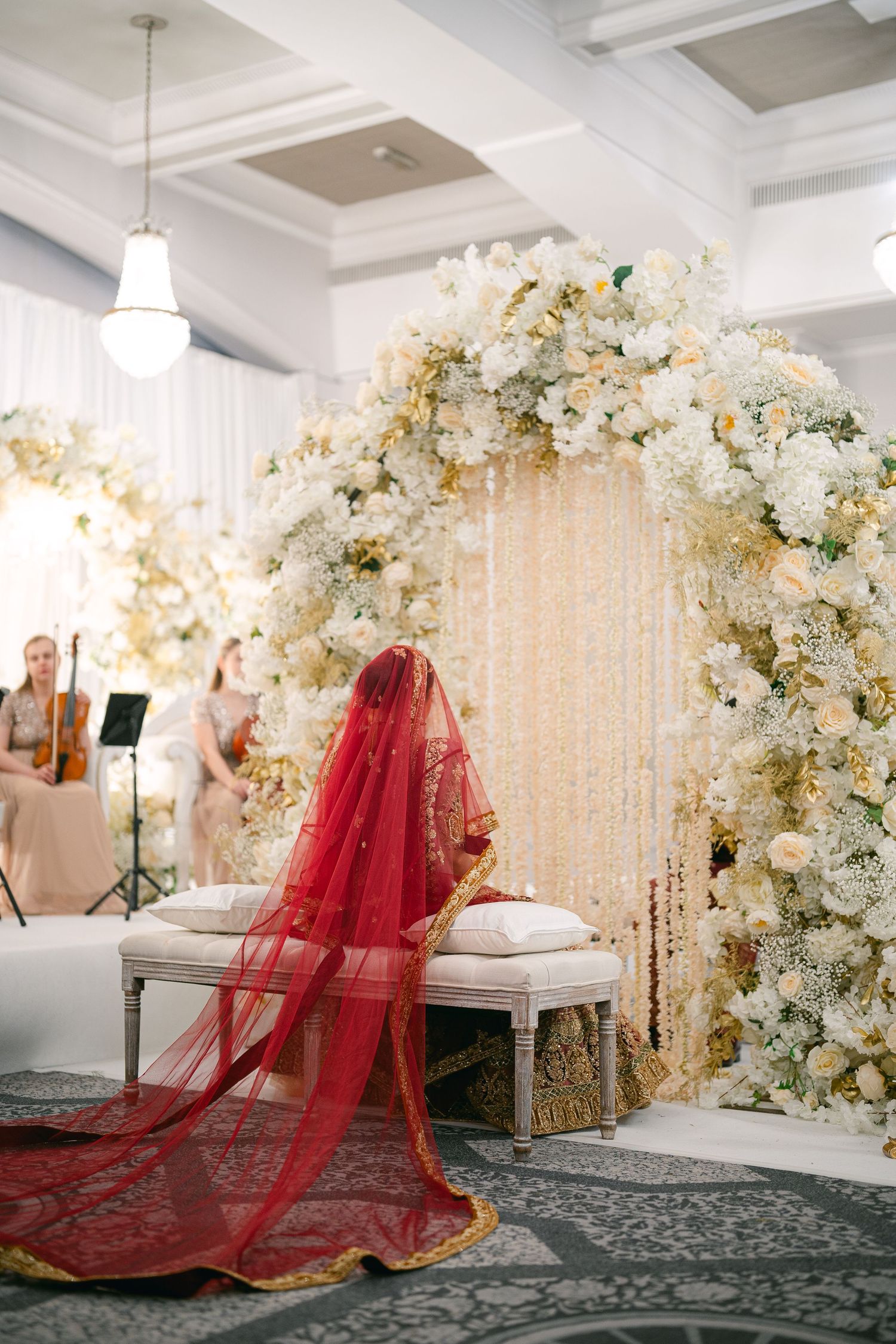 Ornate wedding setup with white floral arrangements and red bridal lehenga against a crystal backdrop.