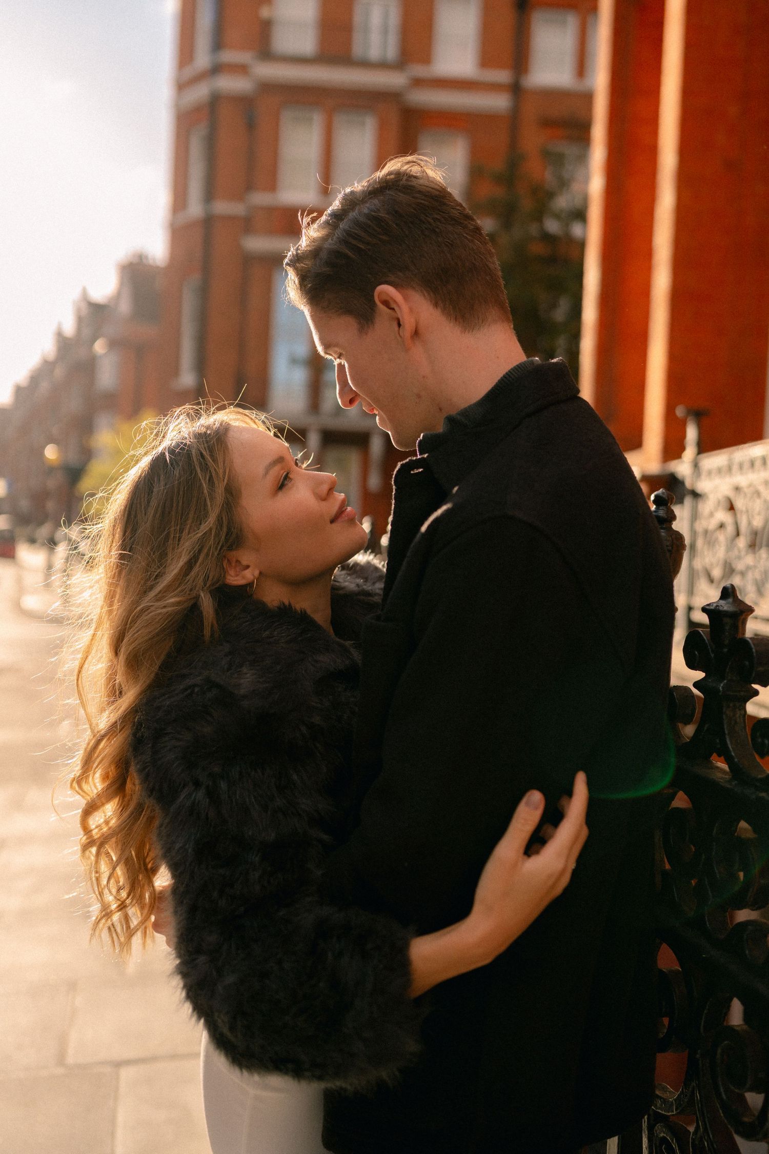 Golden hour photoshoot of couple by brick building with ornate ironwork.