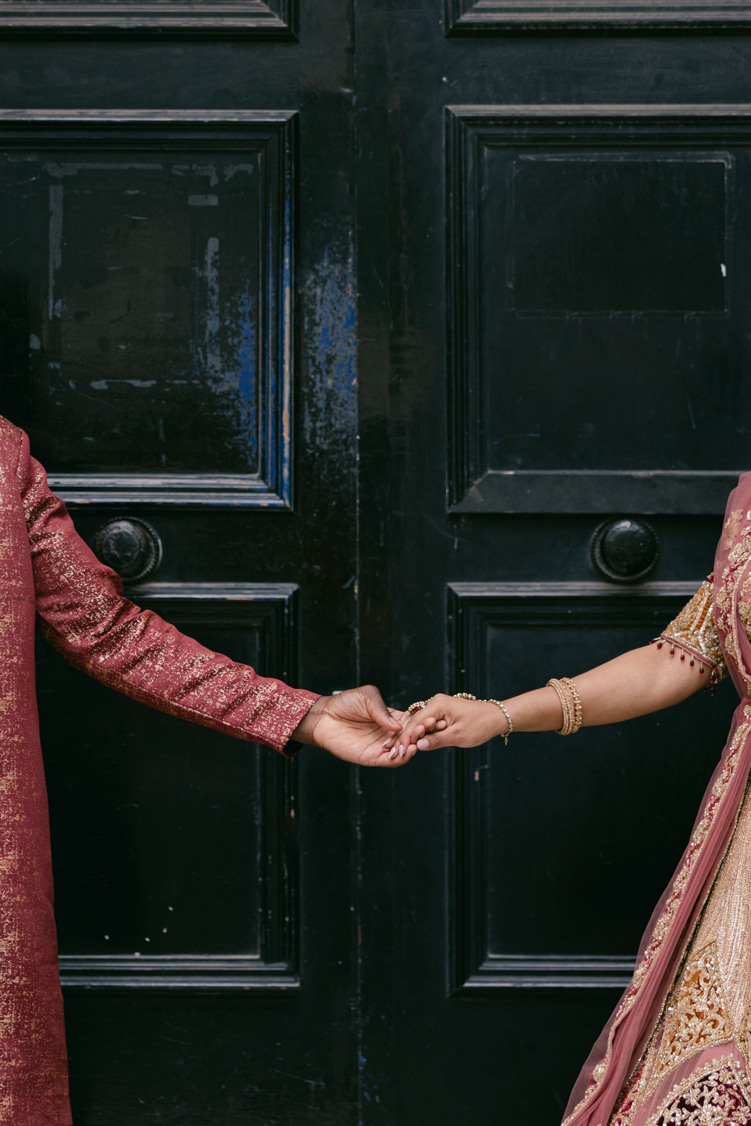 Close-up of hands wearing traditional Indian wedding jewelry against a dark wooden door background.