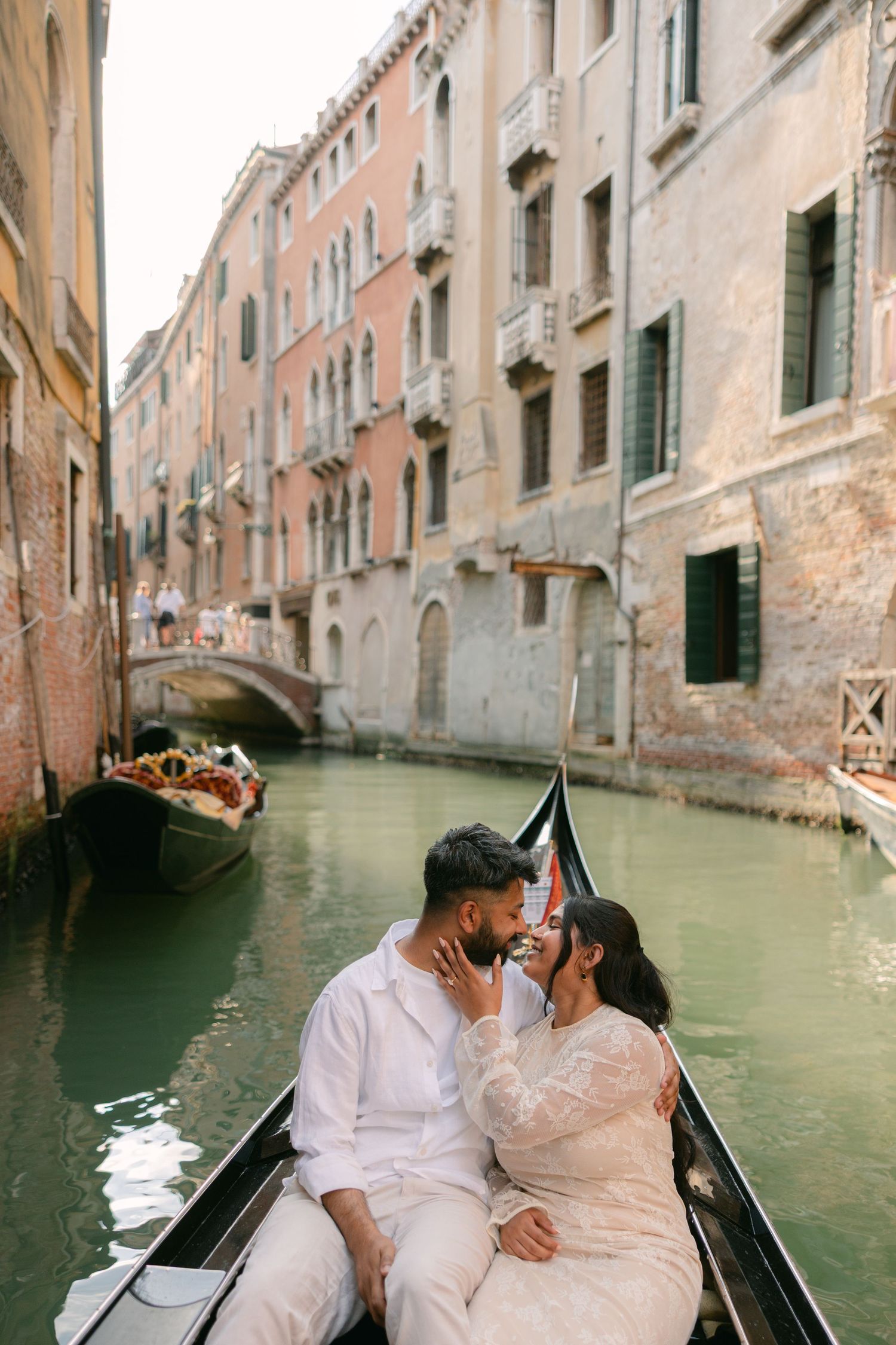 Romantic couple sharing a kiss on a gondola ride through the scenic green canals of Venice, Italy.