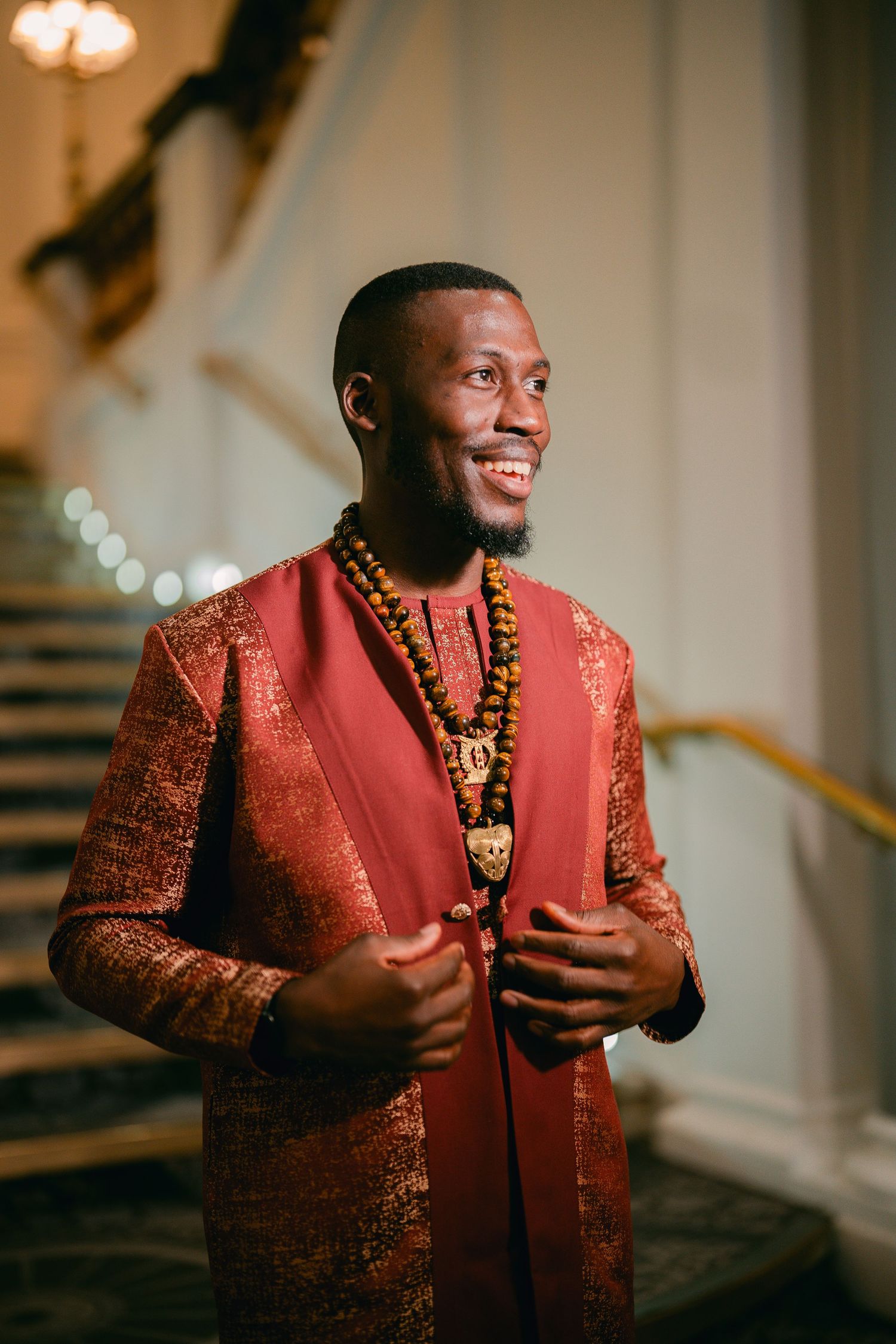 Groom wearing a red and gold traditional outfit with beaded necklace smiling in sequence of photos.