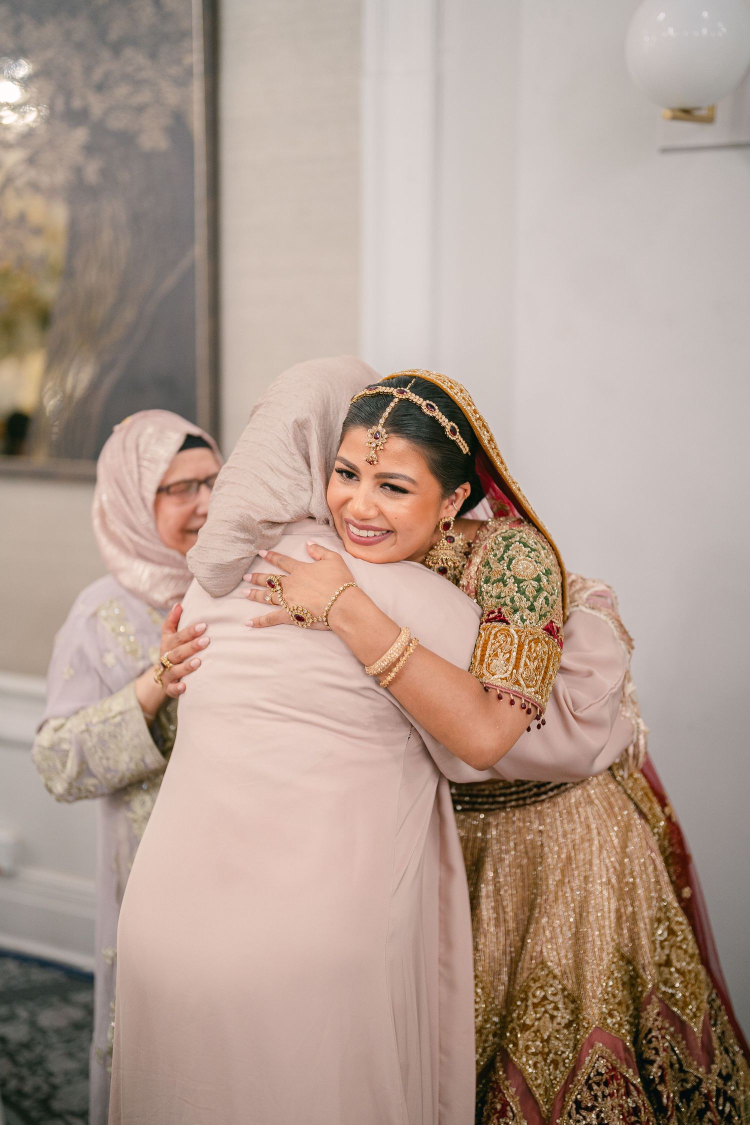 Wedding celebration showing warm embraces between guests in traditional dress against a light interior backdrop.