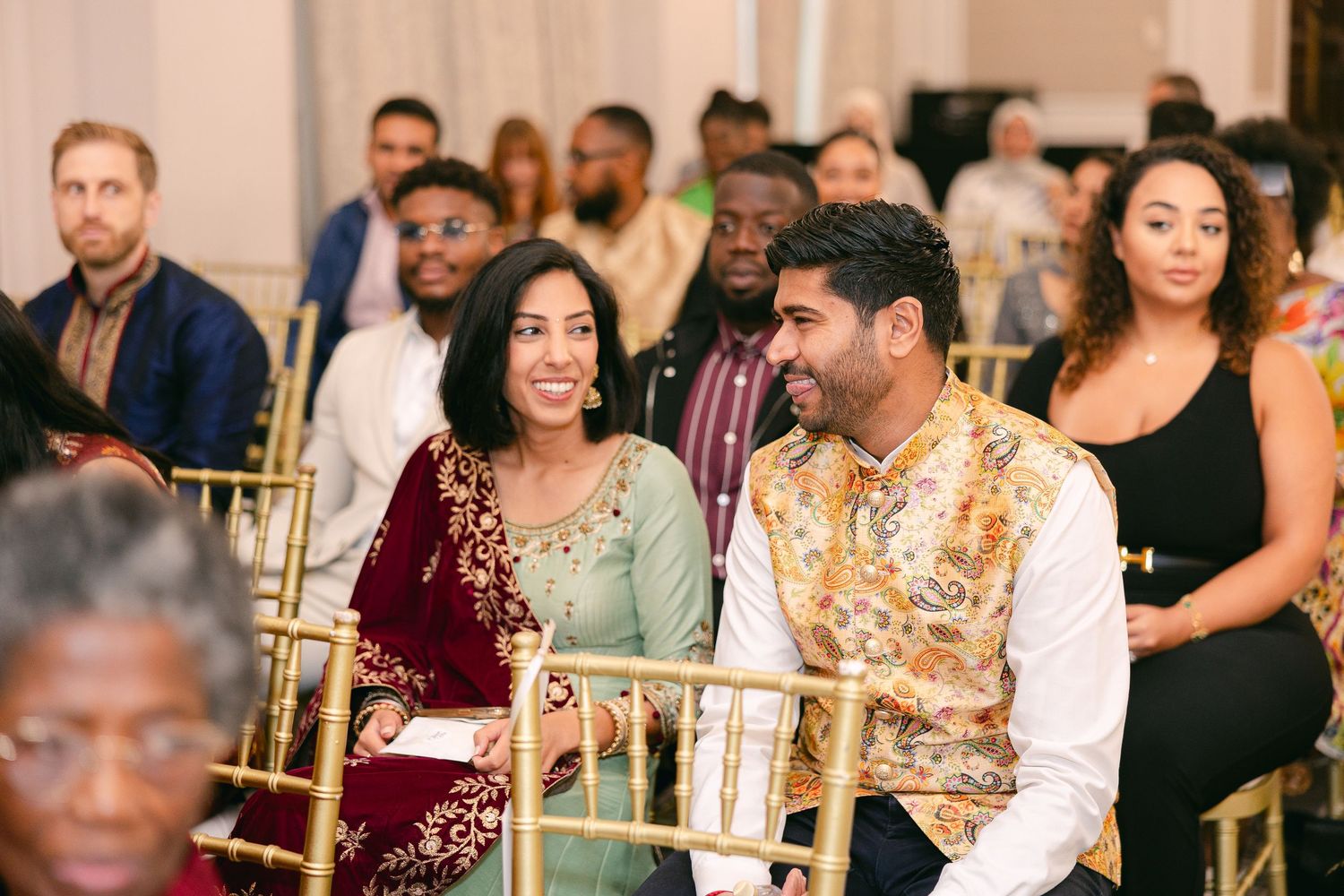A group of guests enjoying a formal celebration in an elegant banquet hall with gold decor and warm lighting.