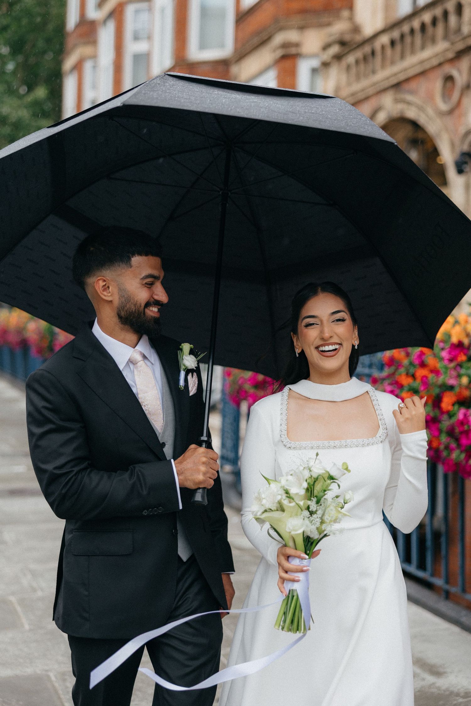 Newlyweds share a joyful moment under black umbrellas during their rainy wedding day celebration.