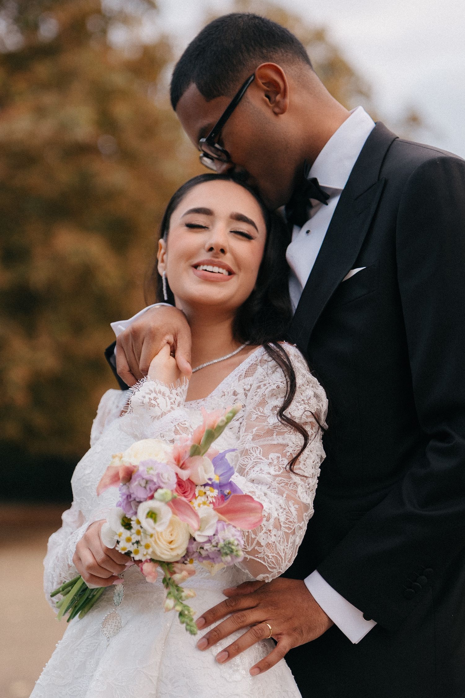 A romantic wedding moment captured outdoors with autumn foliage in the background.