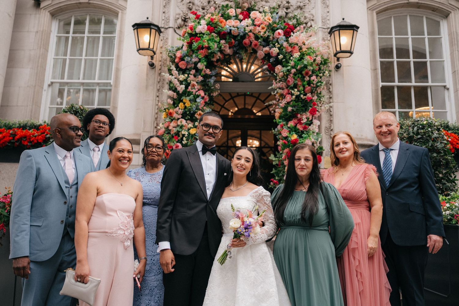 Wedding party poses together in front of floral arch at elegant venue.
