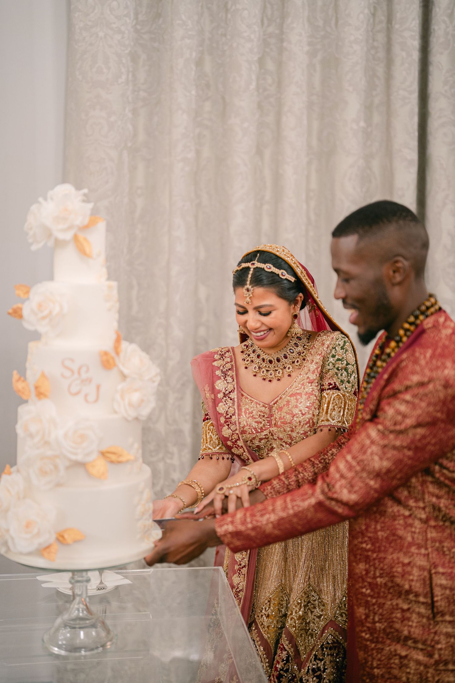A couple in traditional Indian wedding attire cuts their elegant white wedding cake together.