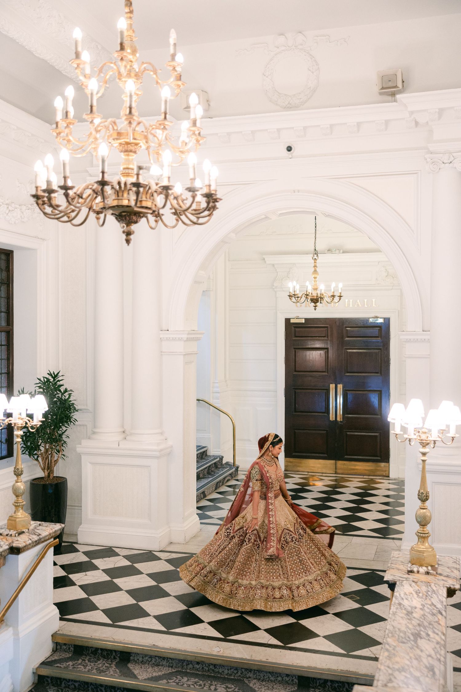 Elegant ballroom with checkerboard floor and crystal chandeliers featuring traditional wedding attire.