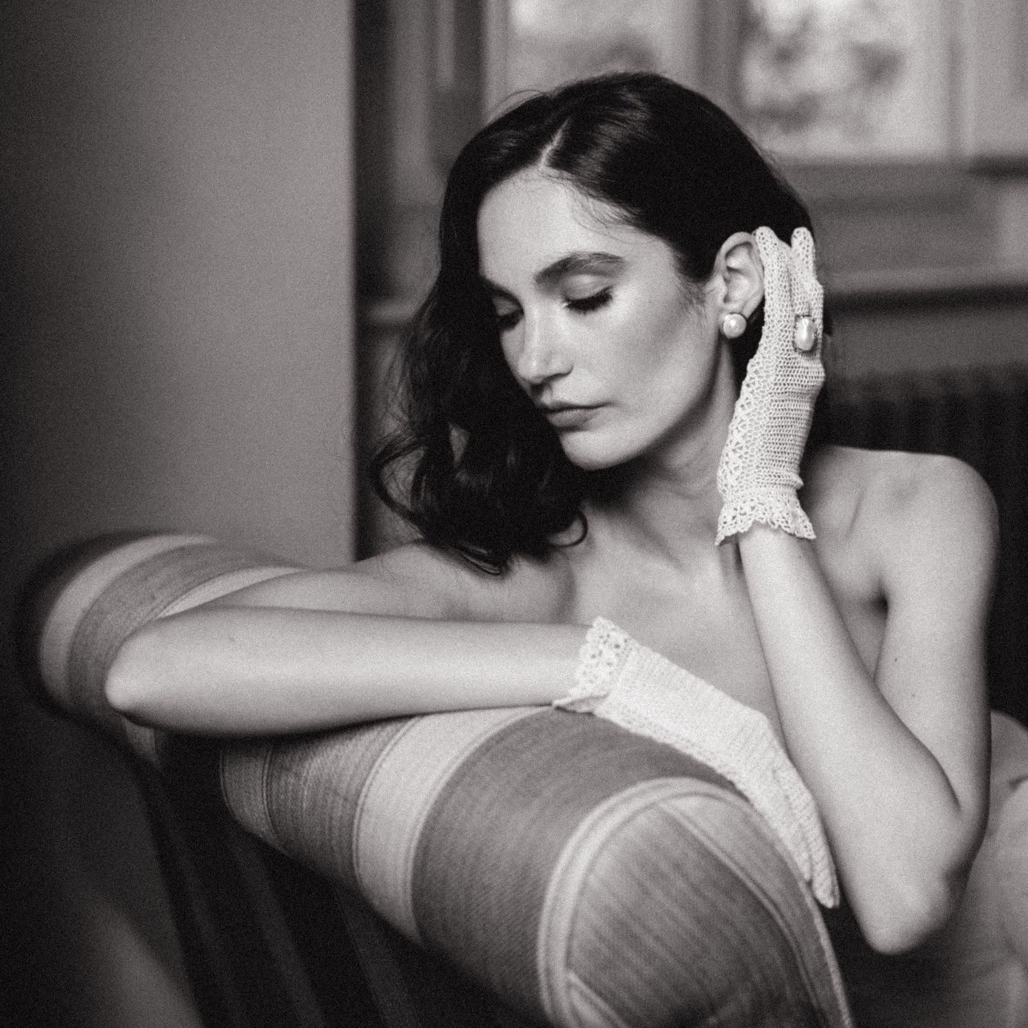 Black and white portrait of an elegant woman in lace gloves, resting her hand near her face in a vintage-inspired pose.