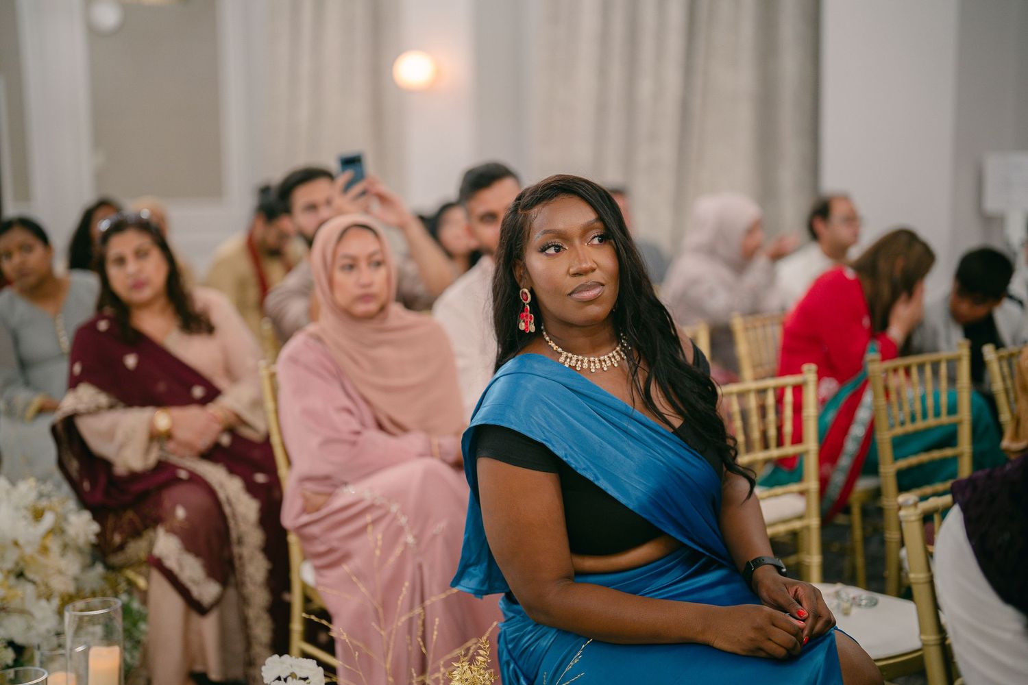 Wedding guests in colorful traditional attire celebrate at an elegant indoor reception venue.