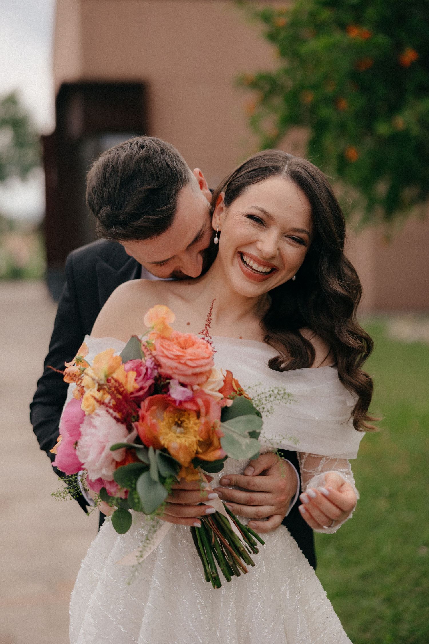 Bride holding colorful bouquet of pink and orange flowers while sharing intimate moment with groom.