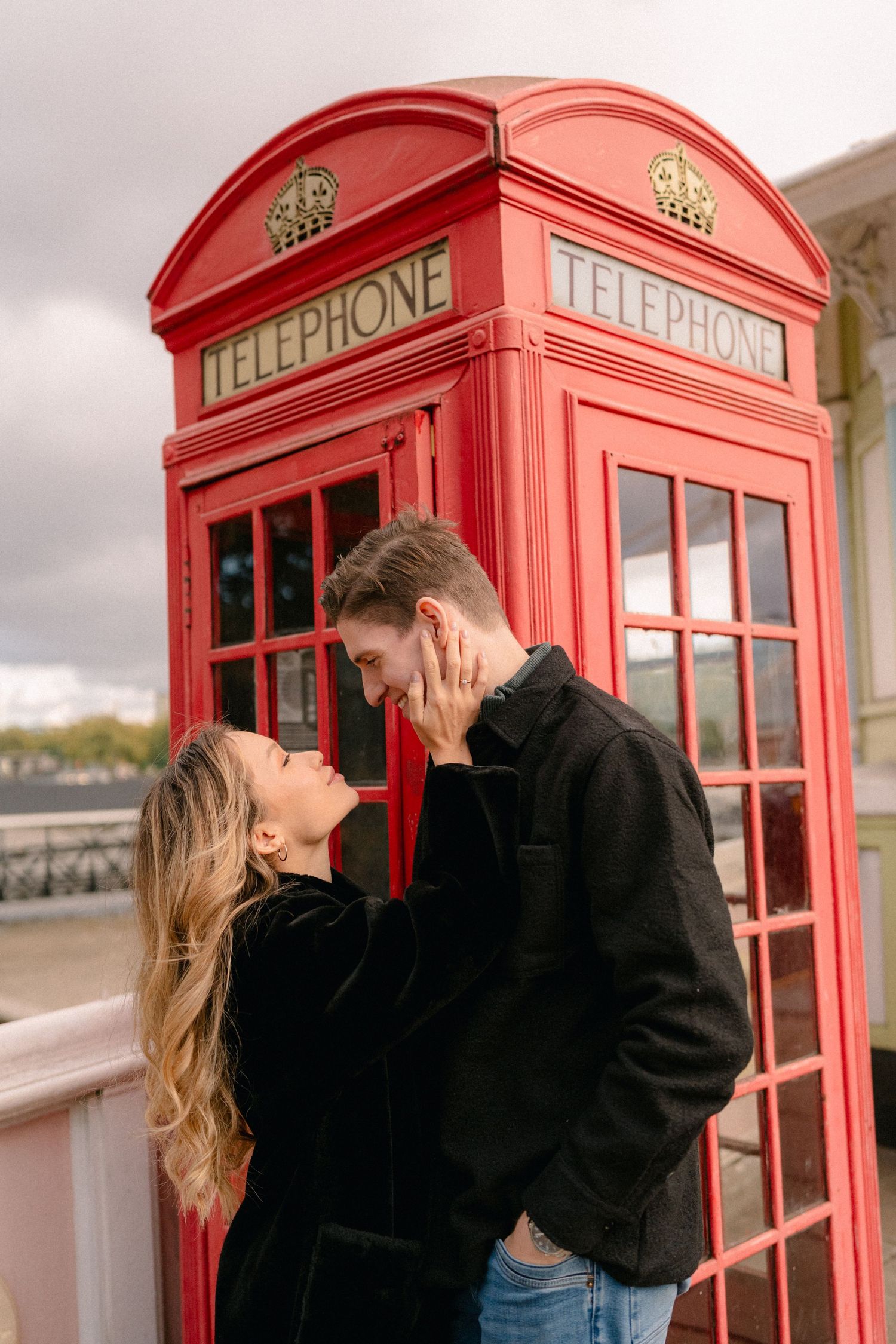 Couple shares romantic moment by iconic red British telephone booth on cloudy day.